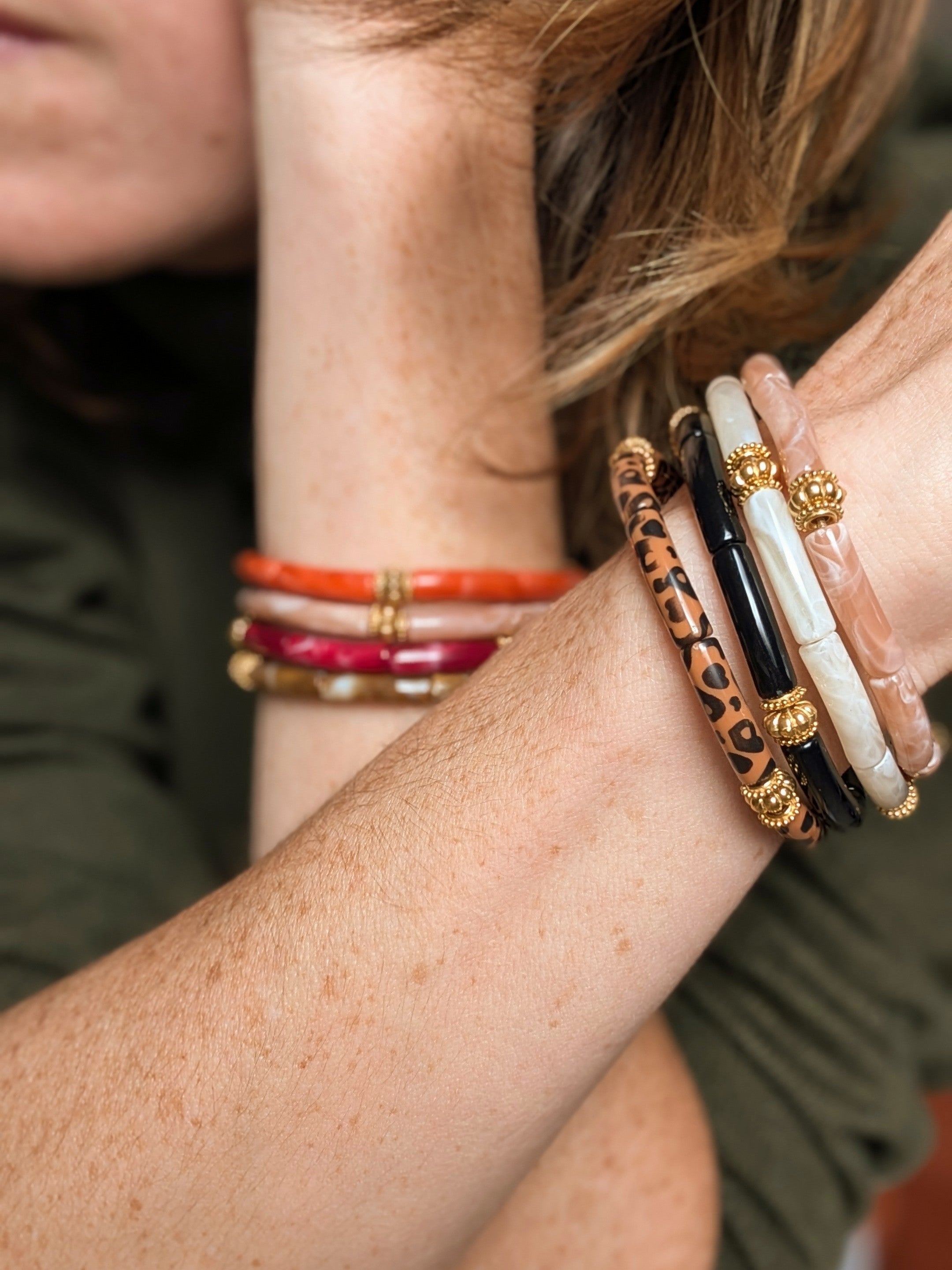 Bracelet June perles tube fin et perles en acier inoxydable doré portés en accumulation au poignet d'une femme. Créations artisanales La Tête dans les Nétoiles