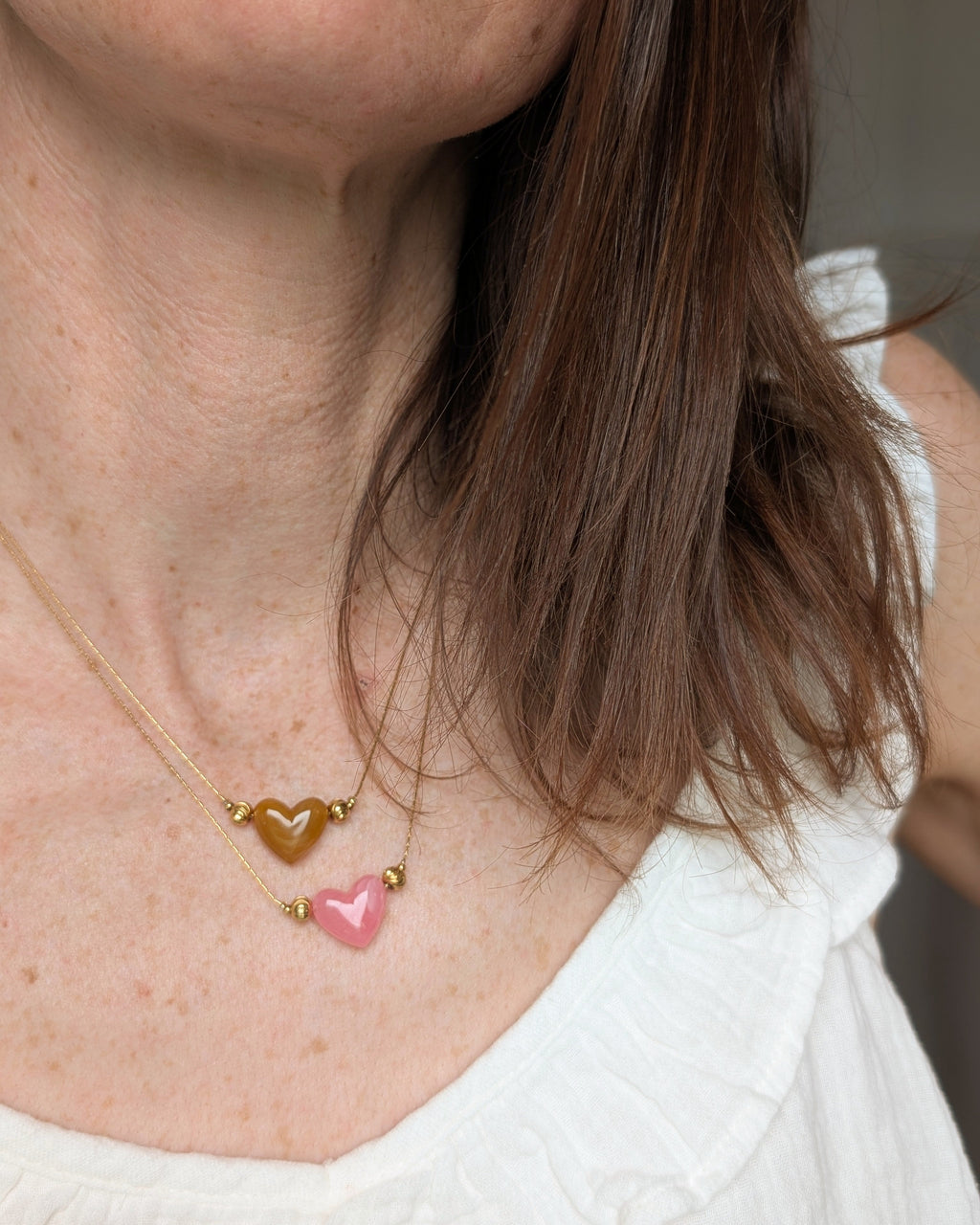 2 Colliers Aimée perle coeur en résine rose tendre et abricot marbré et acier inoxydable doré porté par une femme. Créations artisanales La Tête dans les Nétoiles.