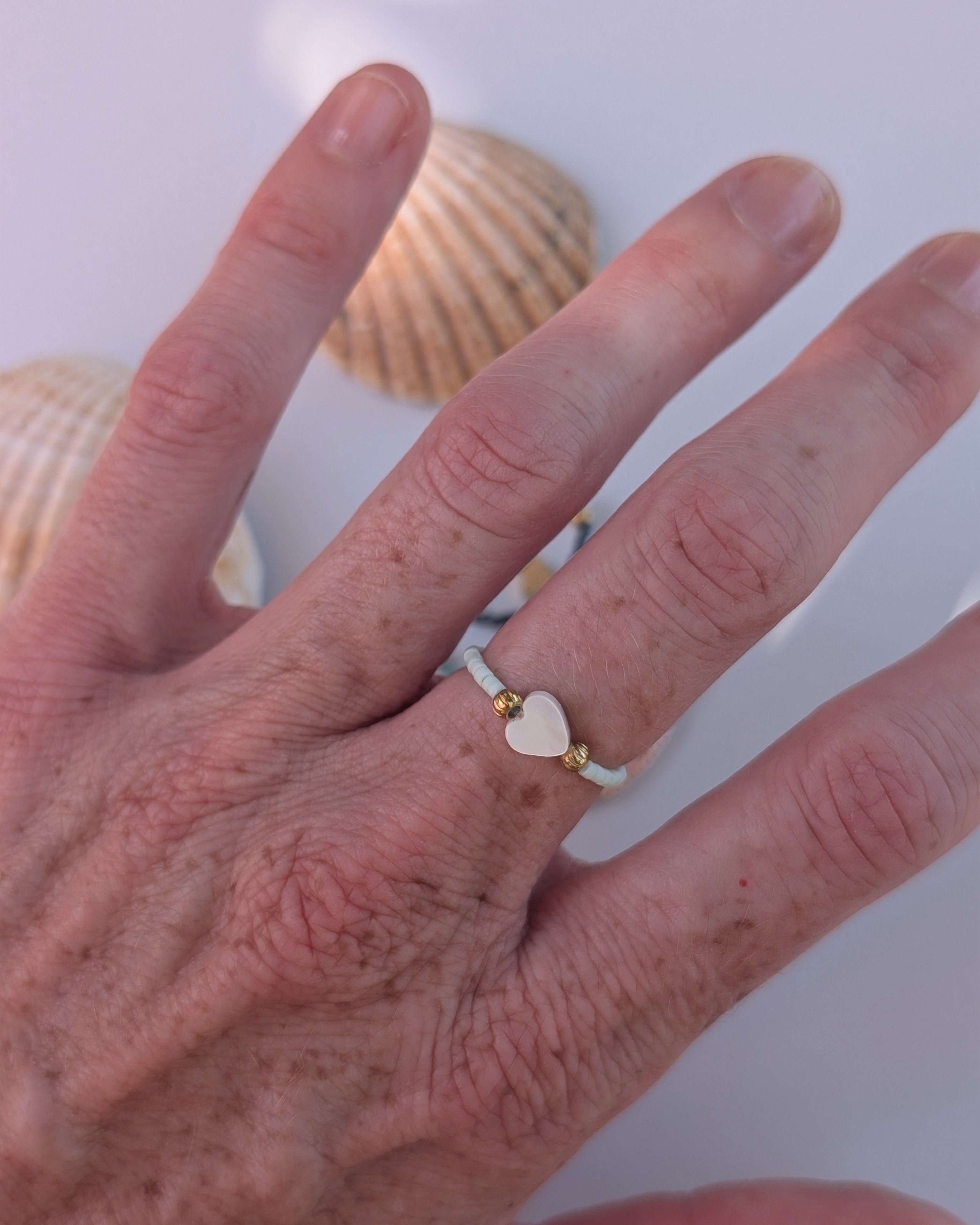 Bague élastique porté par une femme avec perle miyuki et petit coeur en perle de nacre et acier inoxydable. Créations artisanales La Tête dans les nétoiles