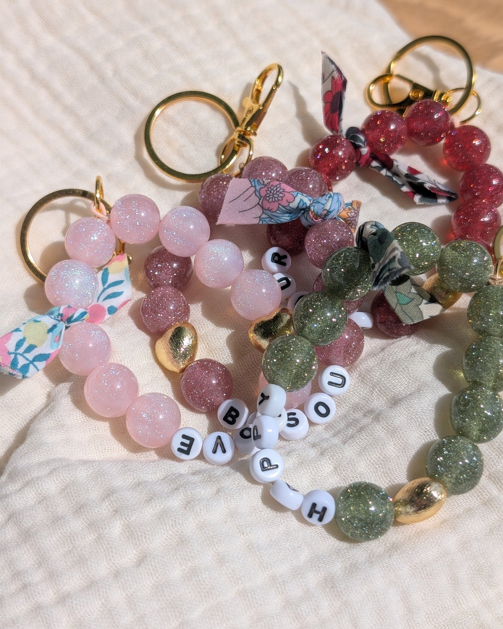Porte clés et bijoux de sac 4 coloris avec perles à paillettes. Posés sur gaze de coton. Créations artisanales La Tête dans les Nétoiles