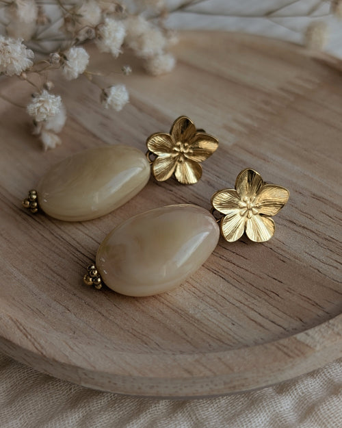 Boucles d'oreilles Jeannette beige rosé gros plan avec fleur dorée sur support bois