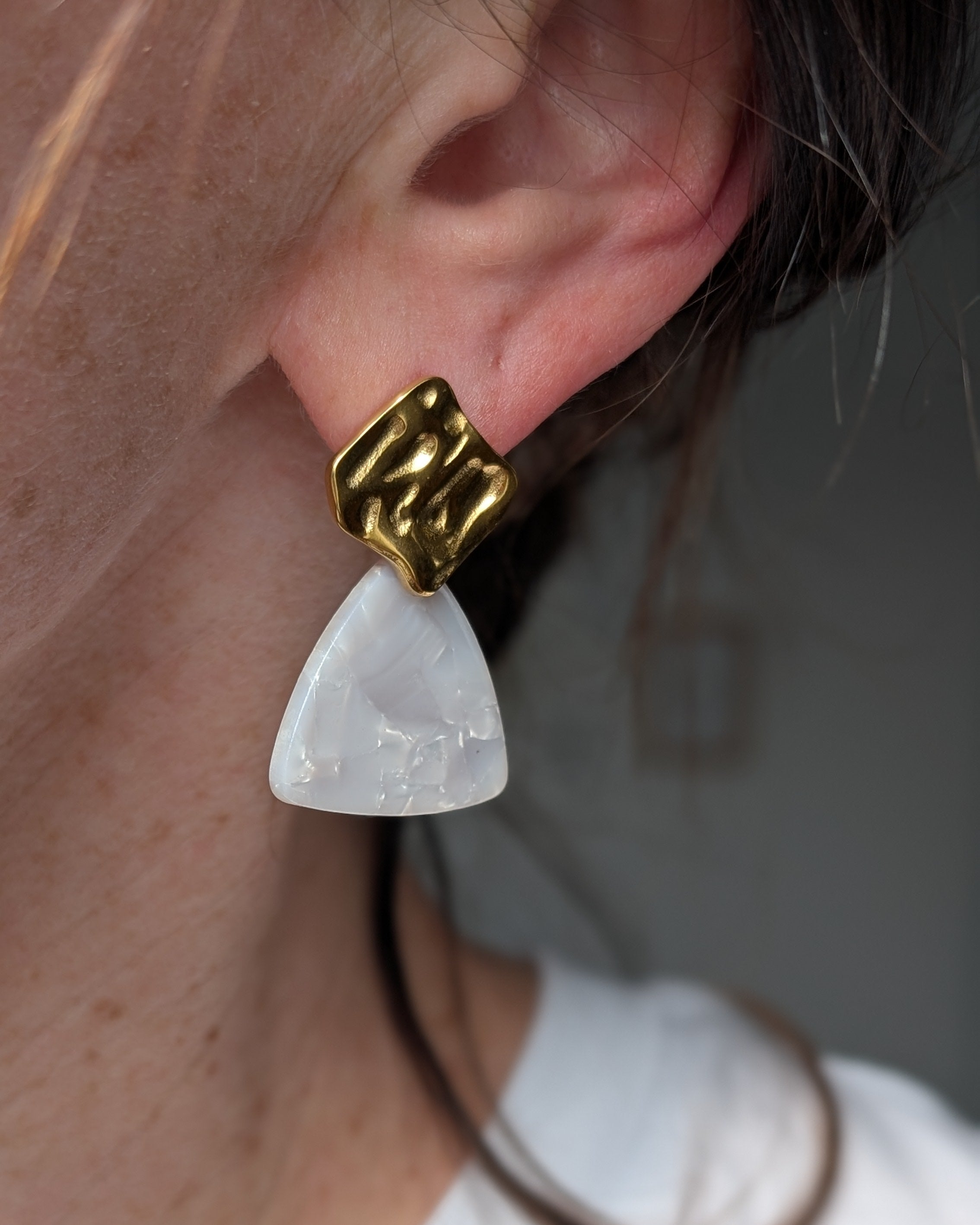 boucles d'oreilles Mae clous d'oreilles froissé en acier et triangle acétate effet marbré perlé blanc. portés par une femme. Création La Tête dans les Nétoiles