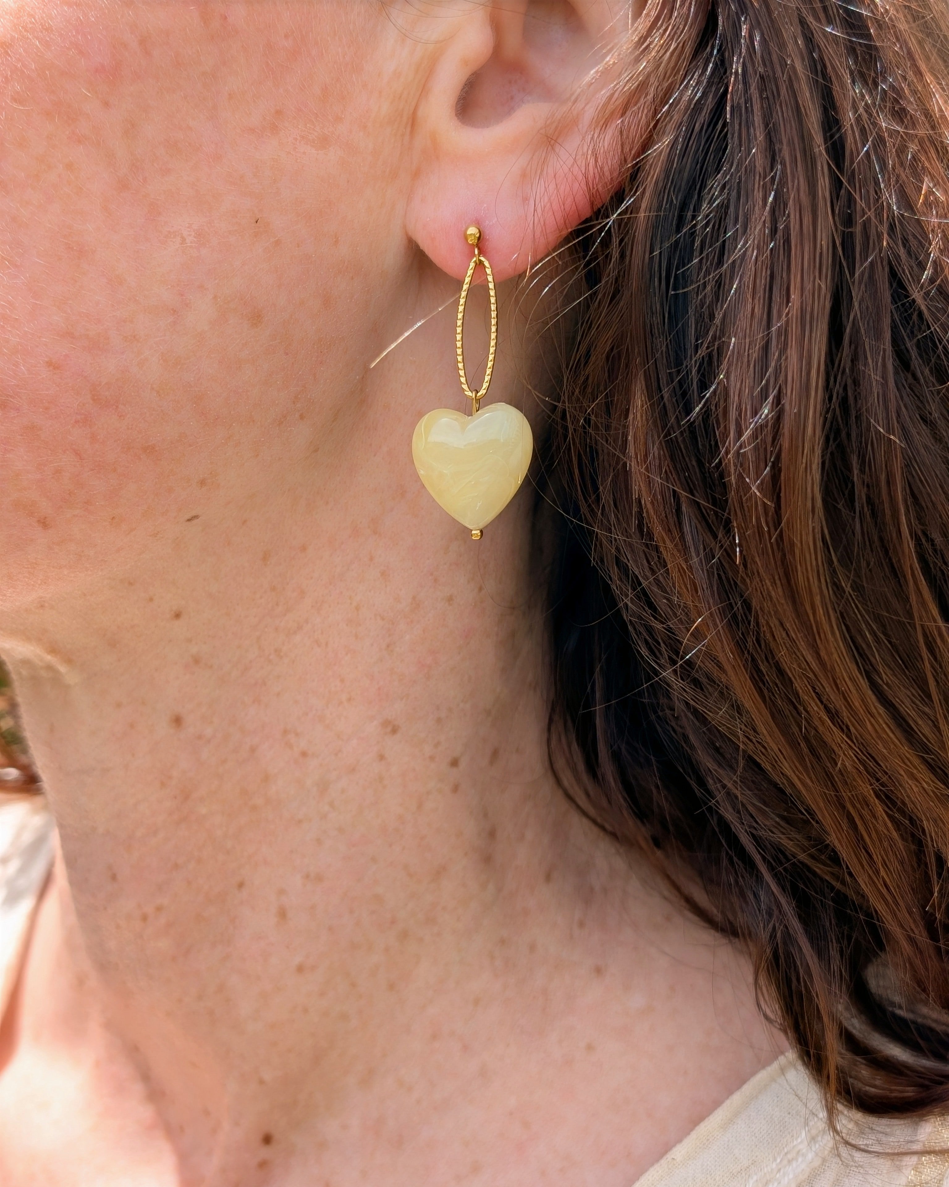 Boucles pendantes Aelia coeur jaune pastel marbrés portées par une femme. Créations artisanales La Tête dans les Nétoiles