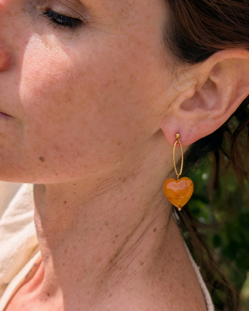 Boucles d'oreilles pendantes Aélia coeur abricot portées par une femme. Création La Tête dans les Nétoiles