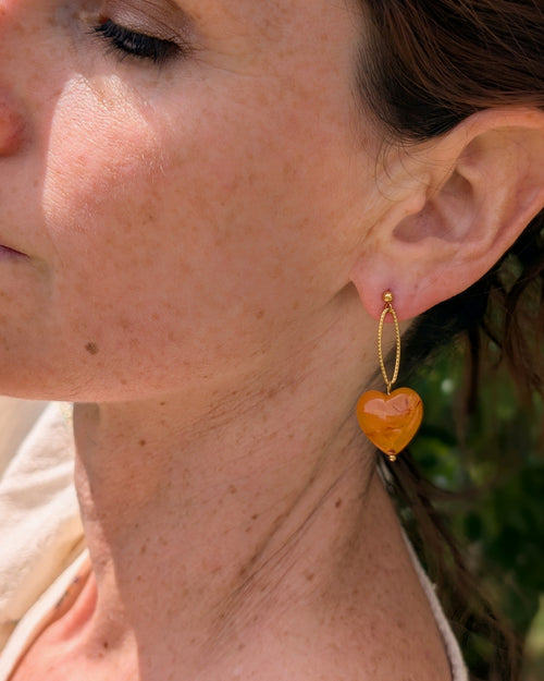 Boucles d'oreilles pendantes Aélia coeur abricot portées par une femme. Création La Tête dans les Nétoiles