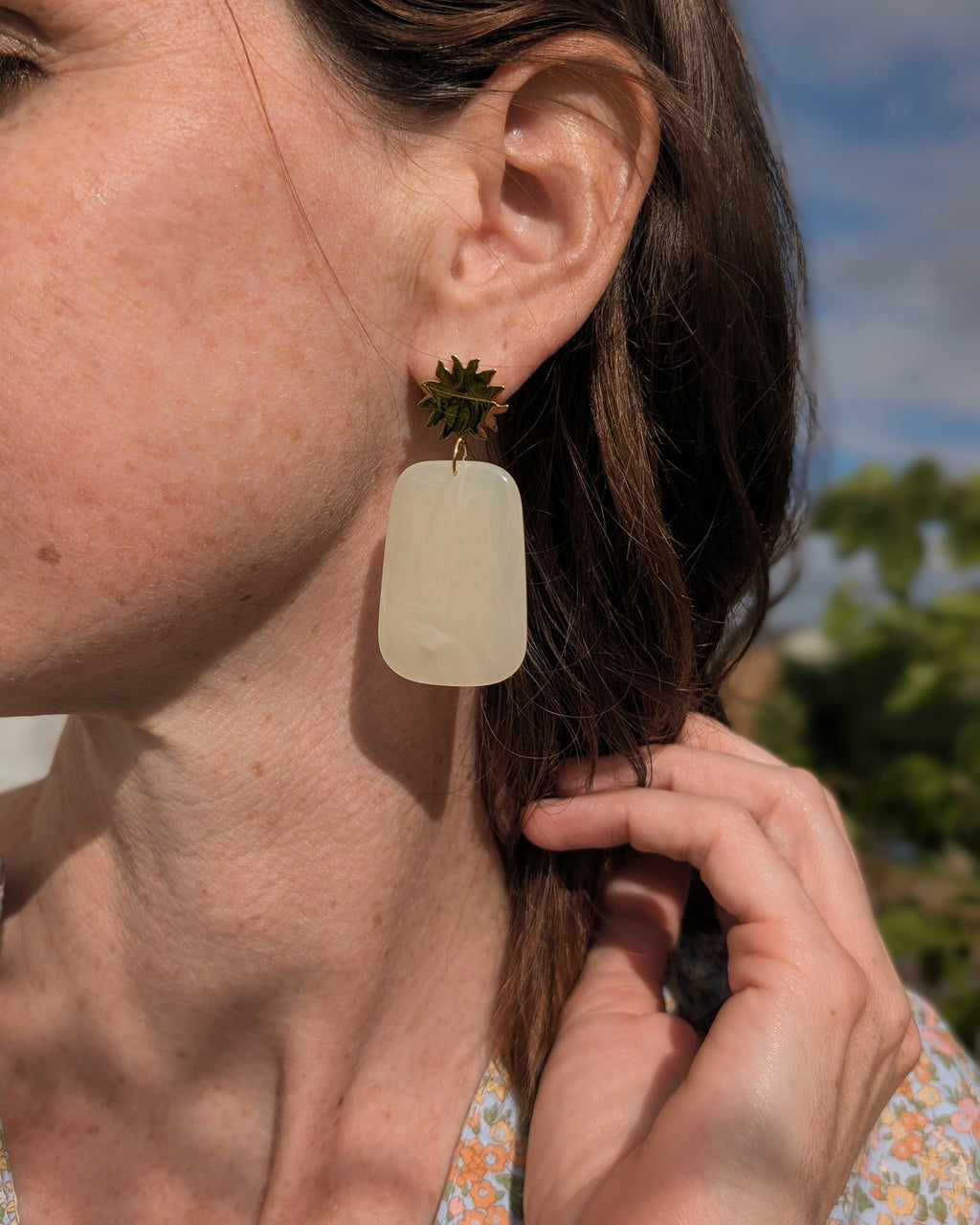 Boucles d'oreilles pendantes soleil et pendentif rectangle résine jaune pastel. Porté par une femme avec une blouse fleurie. Créations artisanales La Tête dans les Nétoiles 