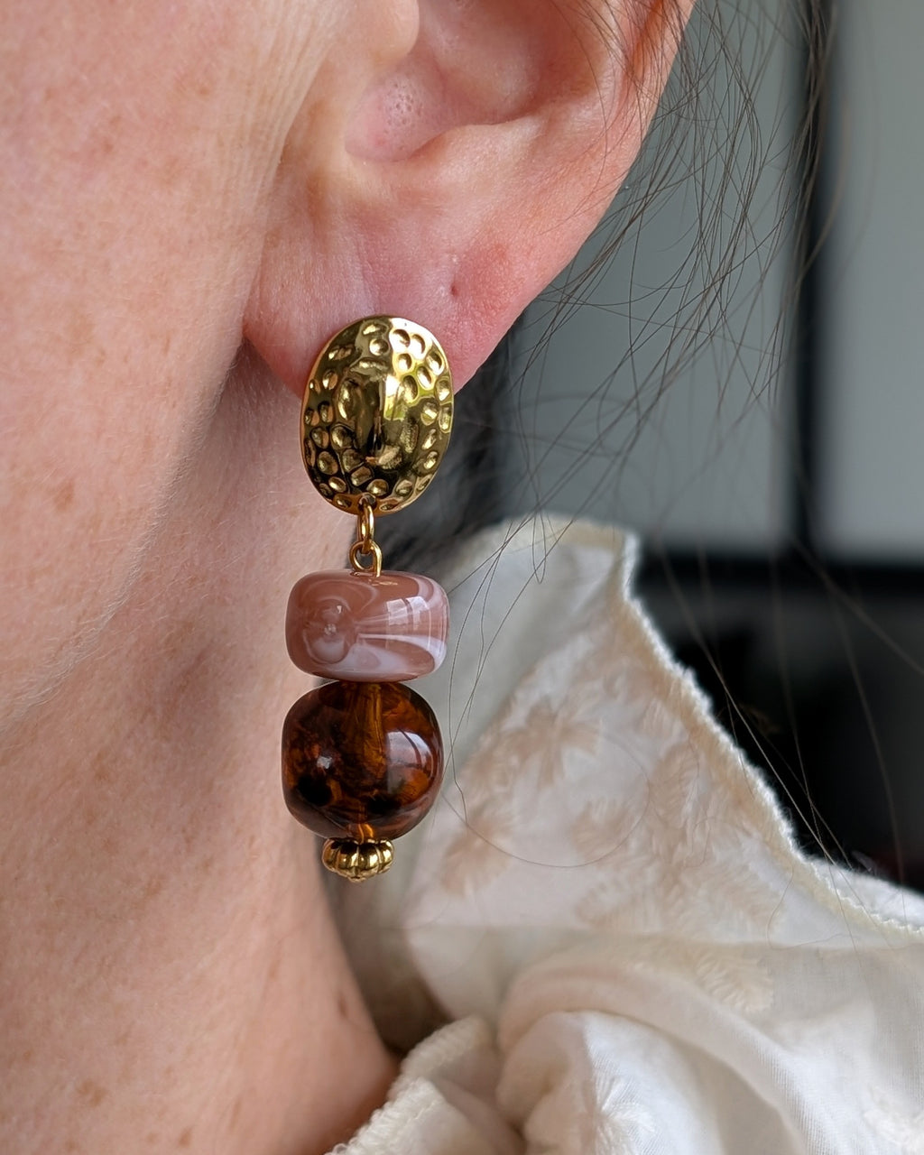 boucles pendantes CHARLIZE clous d'oreilles ovales martelés et perles en résine ambré et terracotta rosé. Portées par une femme Création artisanale La Tête dans les Nétoiles