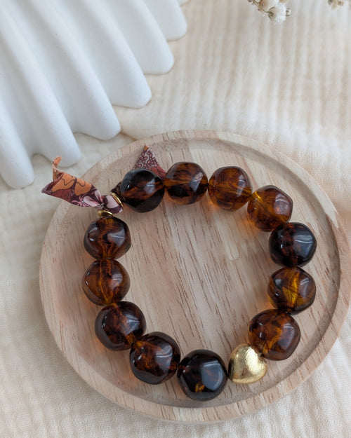 Bracelet Adèle perles résine caramel avec un ruban liberty posé sur un plateau en bois. Créations La Tête dans les Nétoiles
