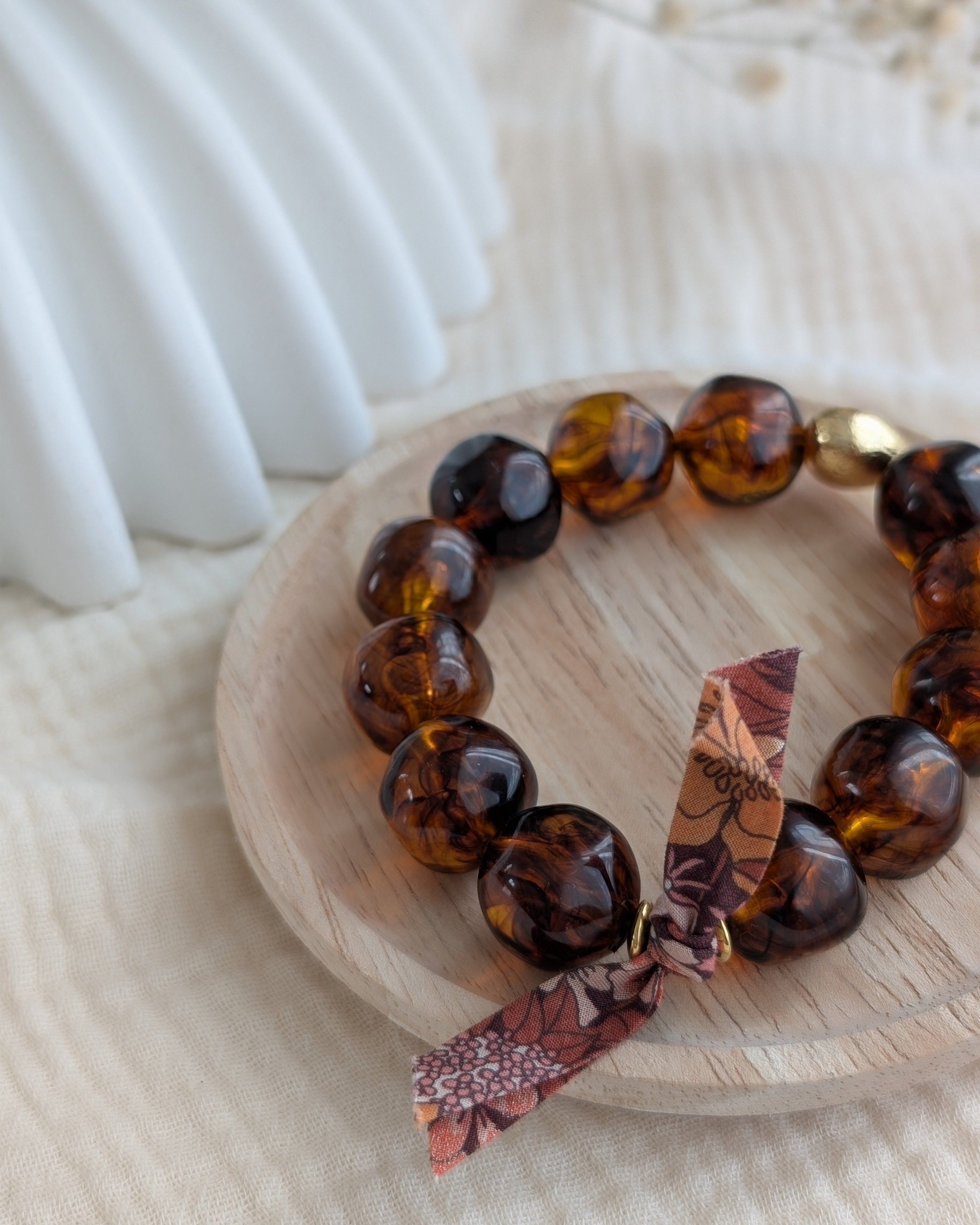 Bracelet Adèle perles résine caramel en gros plan un ruban liberty posé sur un plateau en bois. Créations La Tête dans les Nétoiles