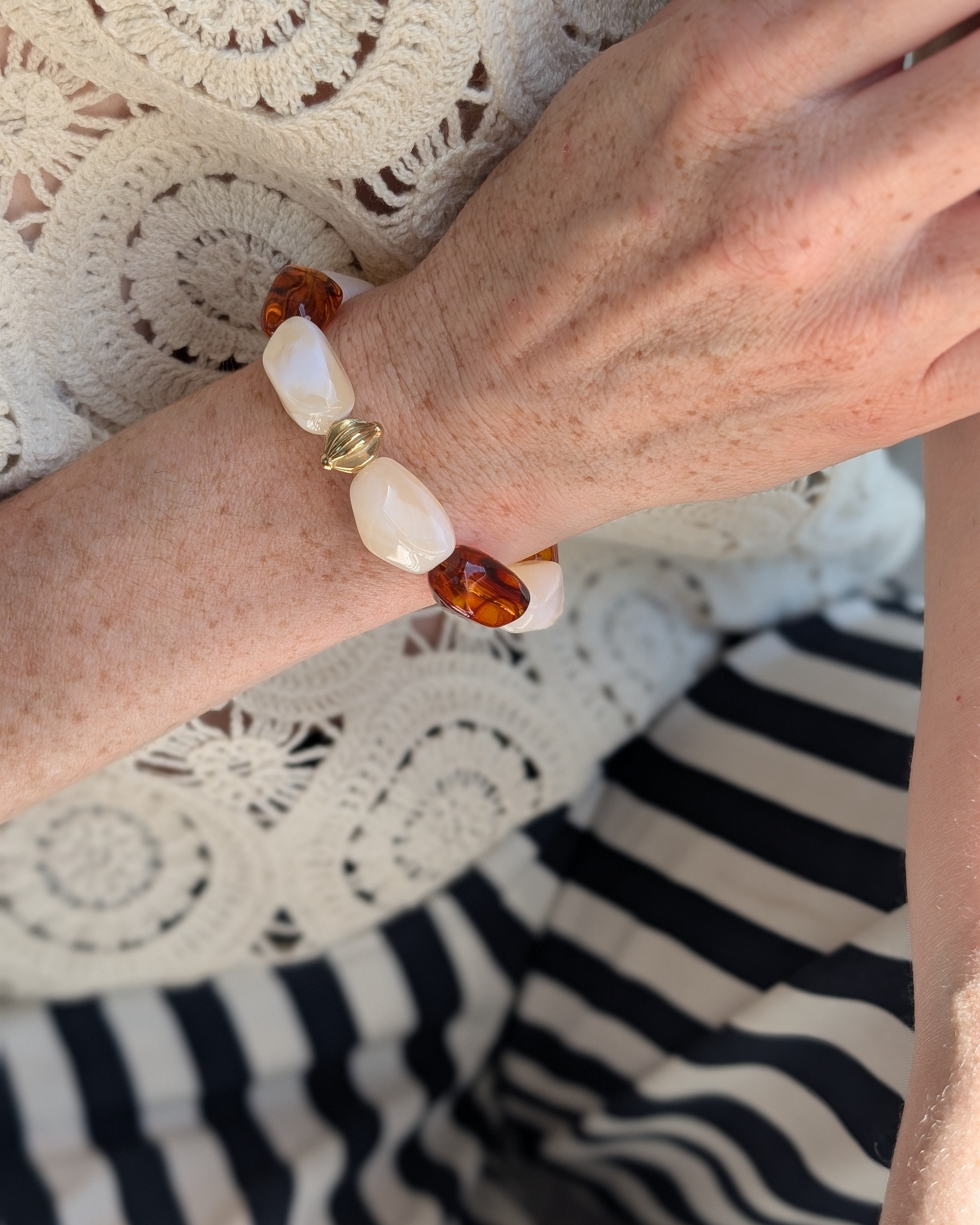 Bracelet Cléa perles résine ambré et crème marbré et acier inoxydable. porté par une femme avec un haut brodé. Créations artisanales La Tête dans les Nétoiles