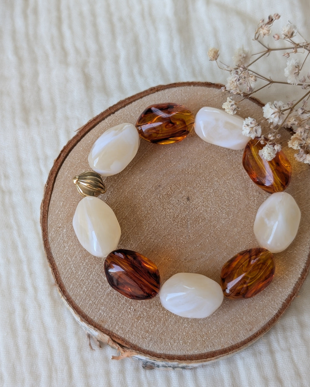 Bracelet Clea perles résine galets irrégulières ambré er crème marbrés . Posé sur rondin en bois. Créations artisanales La Tête dans les Nétoiles
