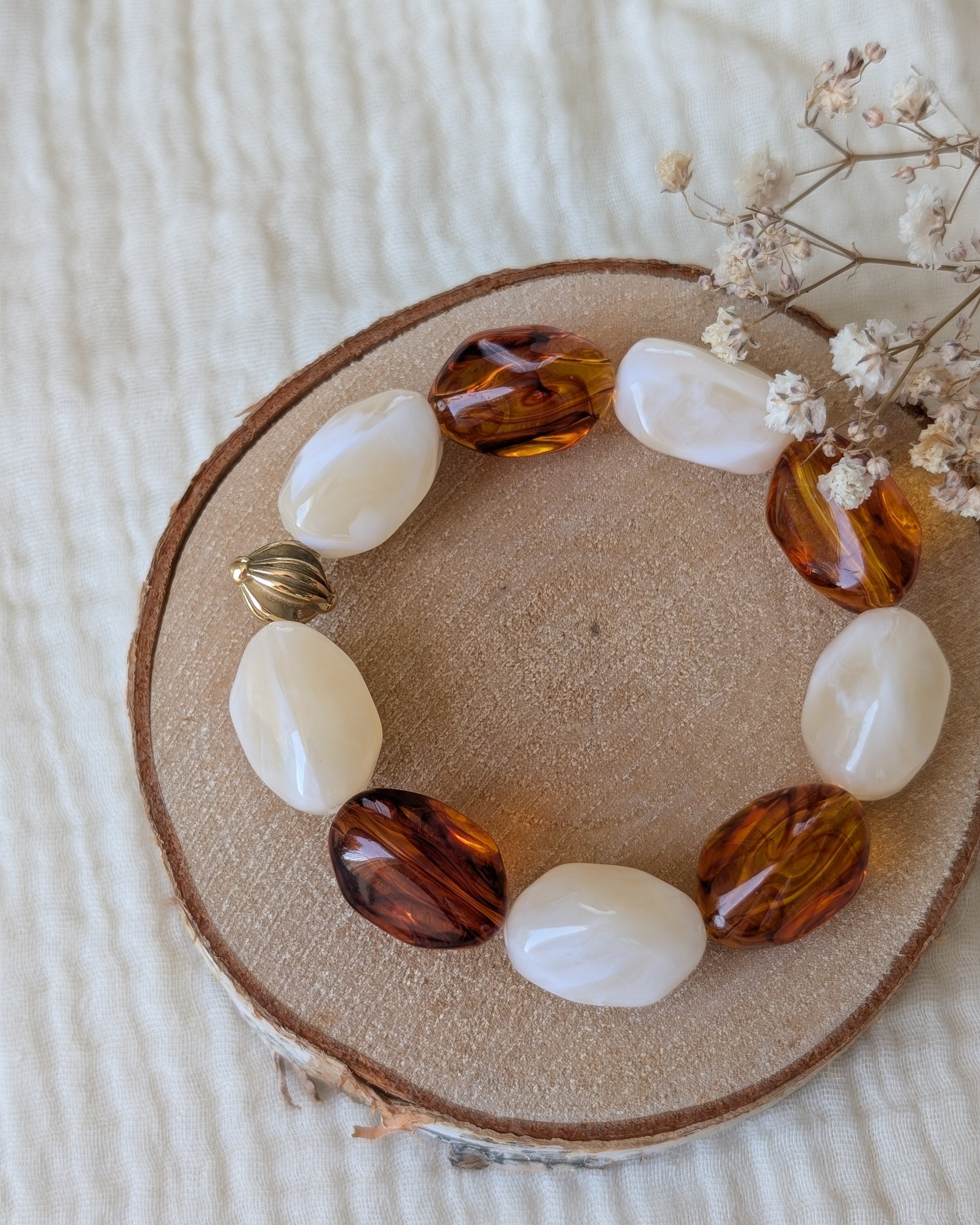 Bracelet Clea perles résine galets irrégulières ambré er crème marbrés . Posé sur rondin en bois. Créations artisanales La Tête dans les Nétoiles