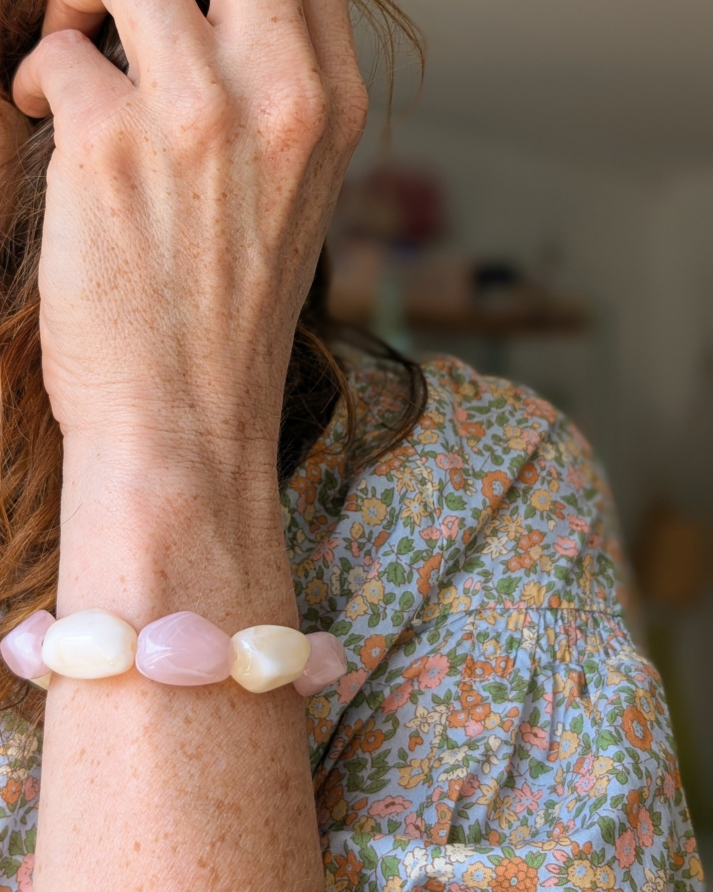 bracelet Clea rose et creme perle en résine. Porté par une femme avec une blouse fleurie. Créations artisanales La Tête dans les nétoiles