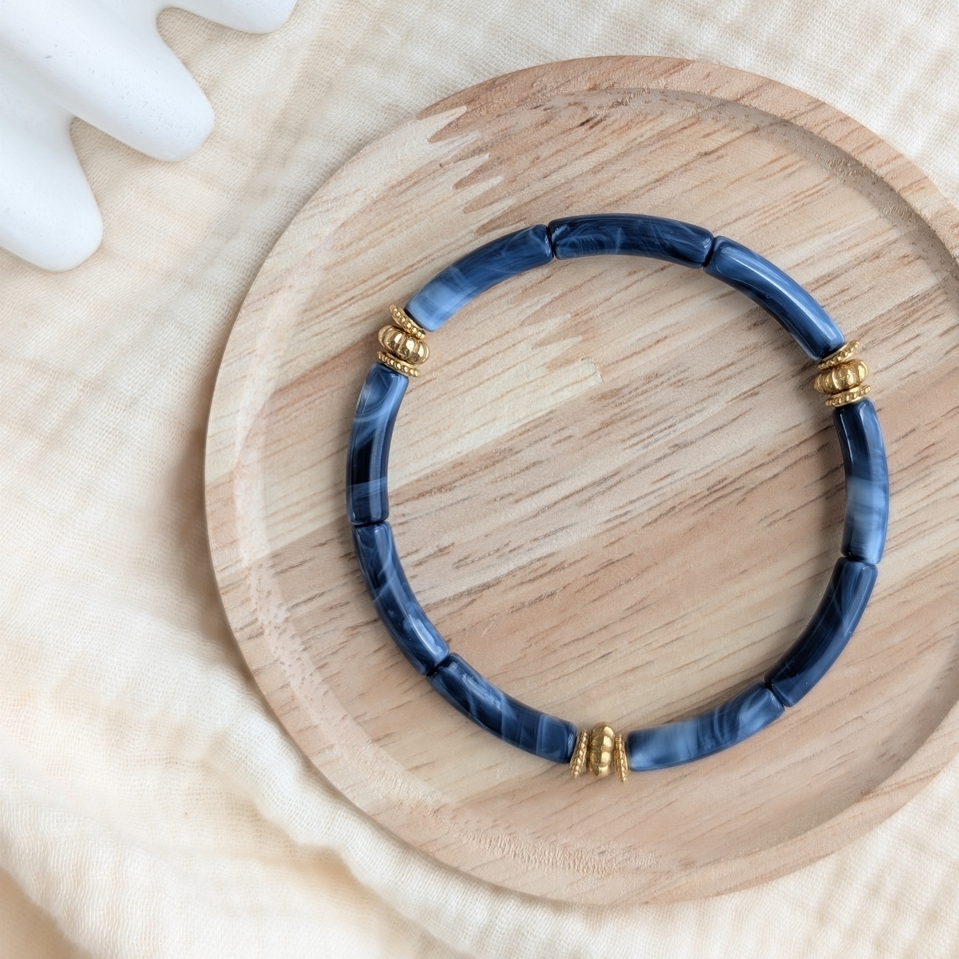 Bracelet JUNE bleu nuit marbré sur support en bois. Perles tubes acryliques et perles dorées en acier inoxydable Création La Tête dans les Nétoiles