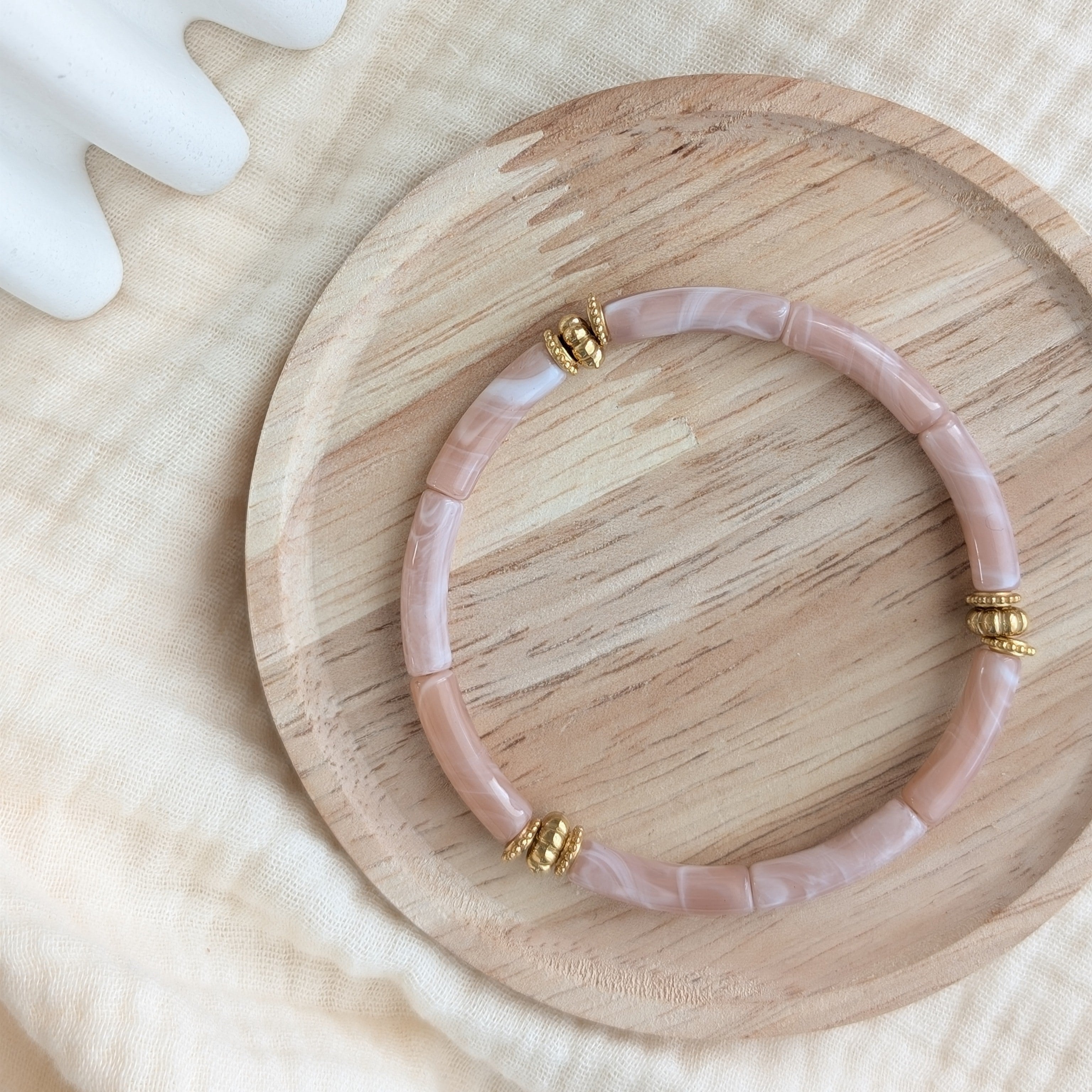 Bracelet JUNE rose nude marbré sur support en bois. Perles tubes acryliques et perles dorées en acier inoxydable Création La Tête dans les Nétoiles