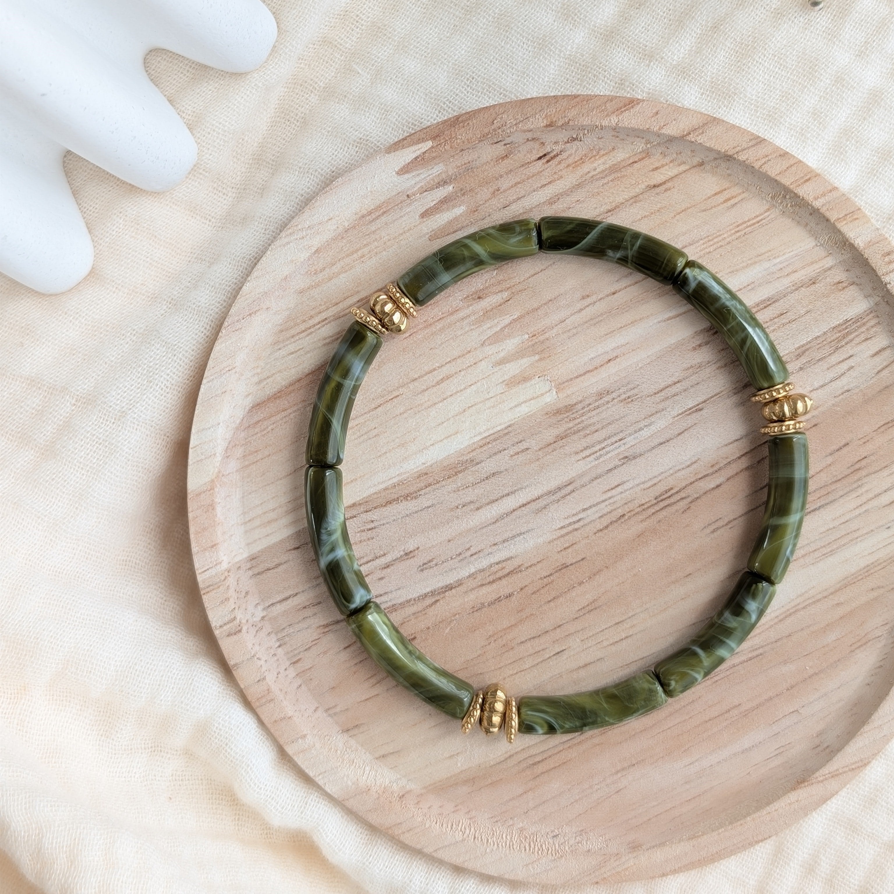 Bracelet JUNE vert olive marbré sur support en bois. Perles tubes acryliques et perles dorées en acier inoxydable Création La Tête dans les Nétoiles