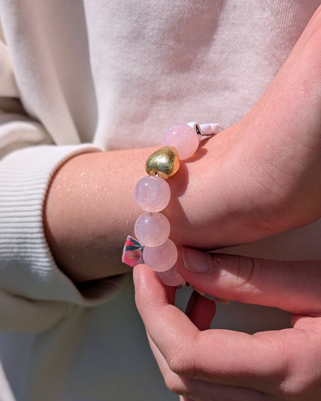 Bracelet perle à paillettes rose clair orné d'un ruban liberty porté par une petite fille gros plan sur le coeur. Créations fait main La Tête dans les Nétoiles