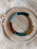 Bracelet Lisa Tons de vert posé sur un support en bois. Perle tube en résine et acrylique créations La Tête dans les Nétoiles.