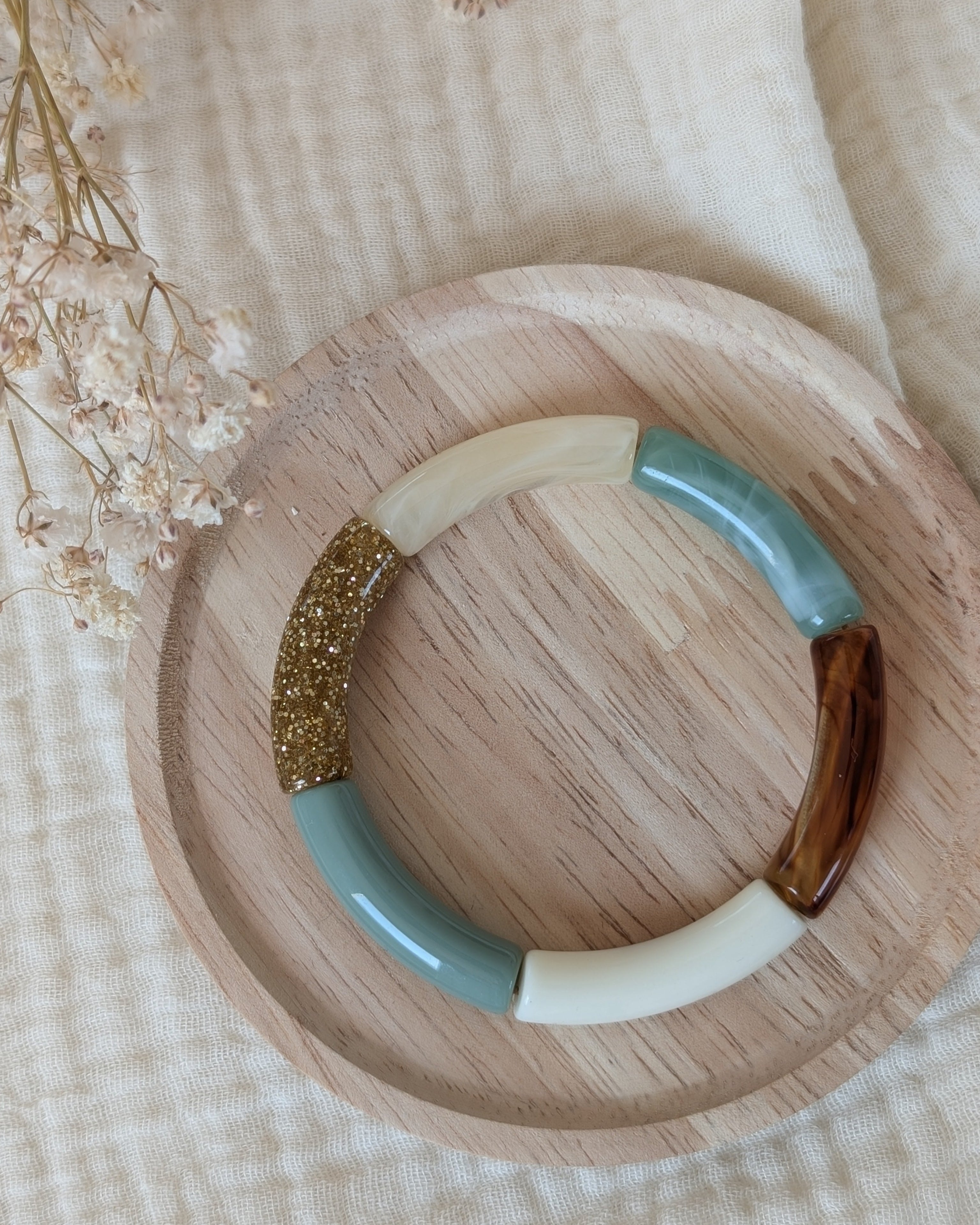 Bracelet Lisa perle tube vert sauge et marbré et glitter. Posé sur support en bois. Création La Tête dans les nétoiles