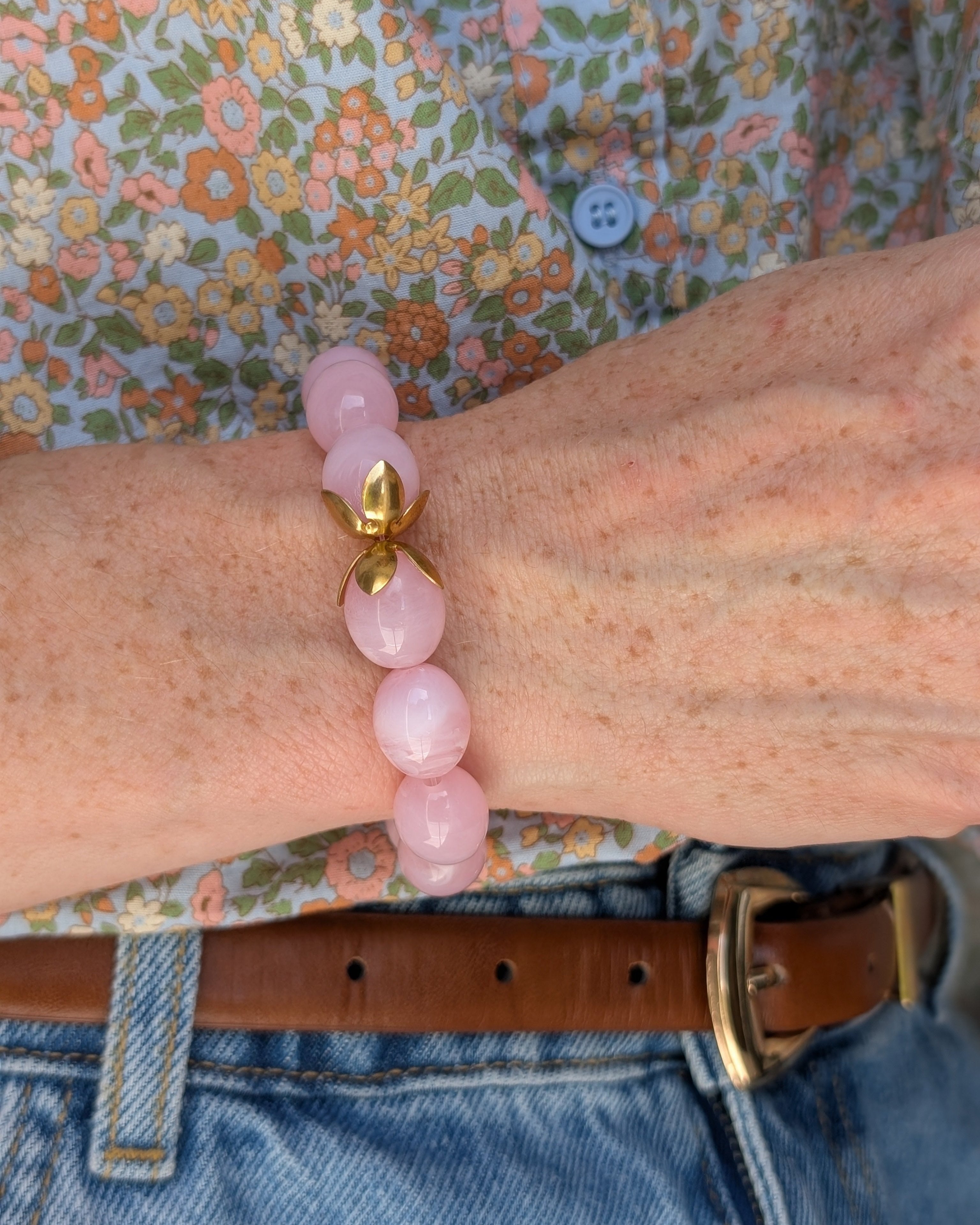 Bracelet Olivia rose poudré marbré porté au poignet d'une femme avec blouse fleurie. perles enr ésine et coupellees fleuries en acier inoxydable. Créations artisanales La Tête dans les Nétoiles