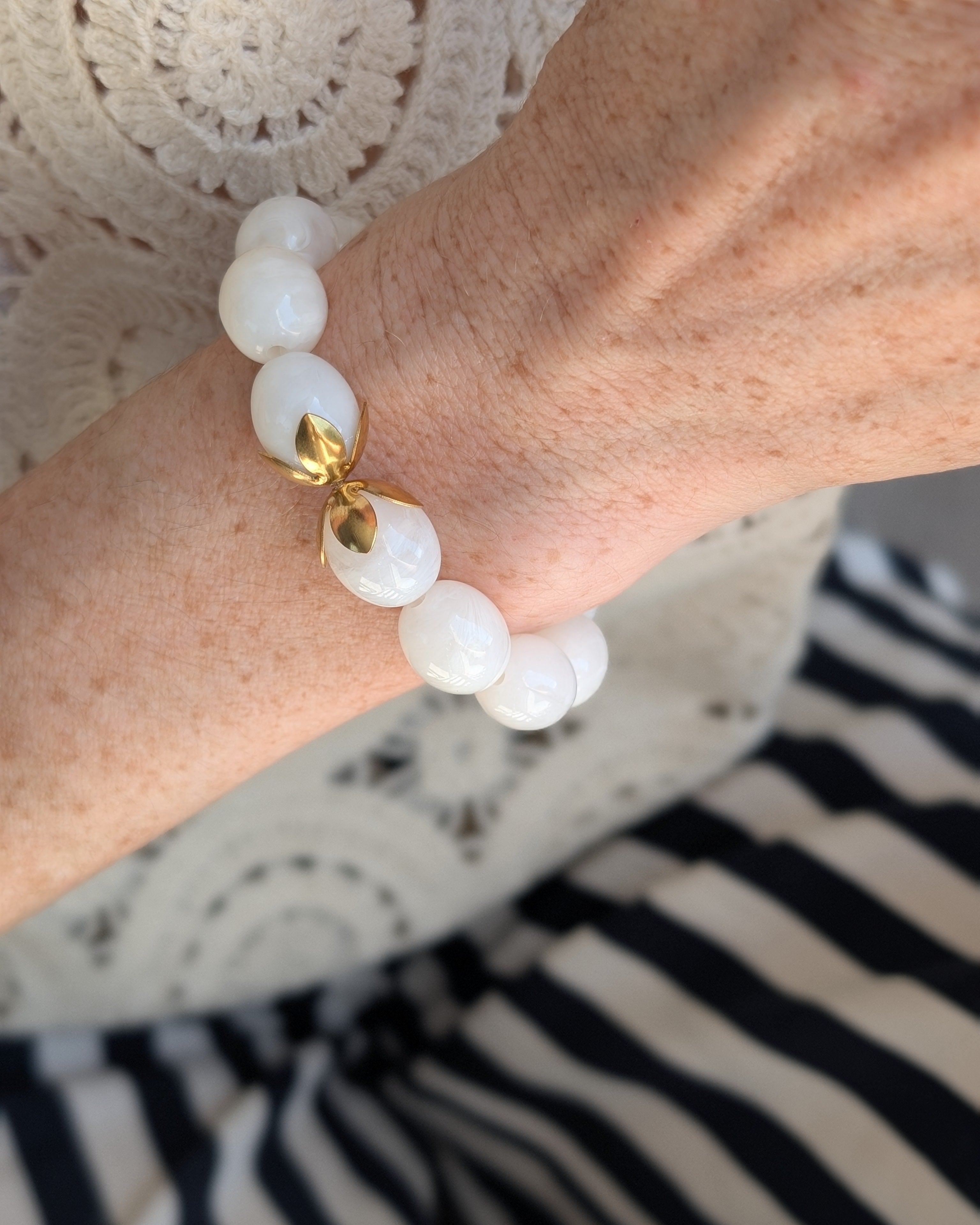 Bracelet Olivia porté en gros plan perles résine blanc marbré avec haut brodé et pantalon à rayures. Créations artisanales La Tête dans les Nétoiles