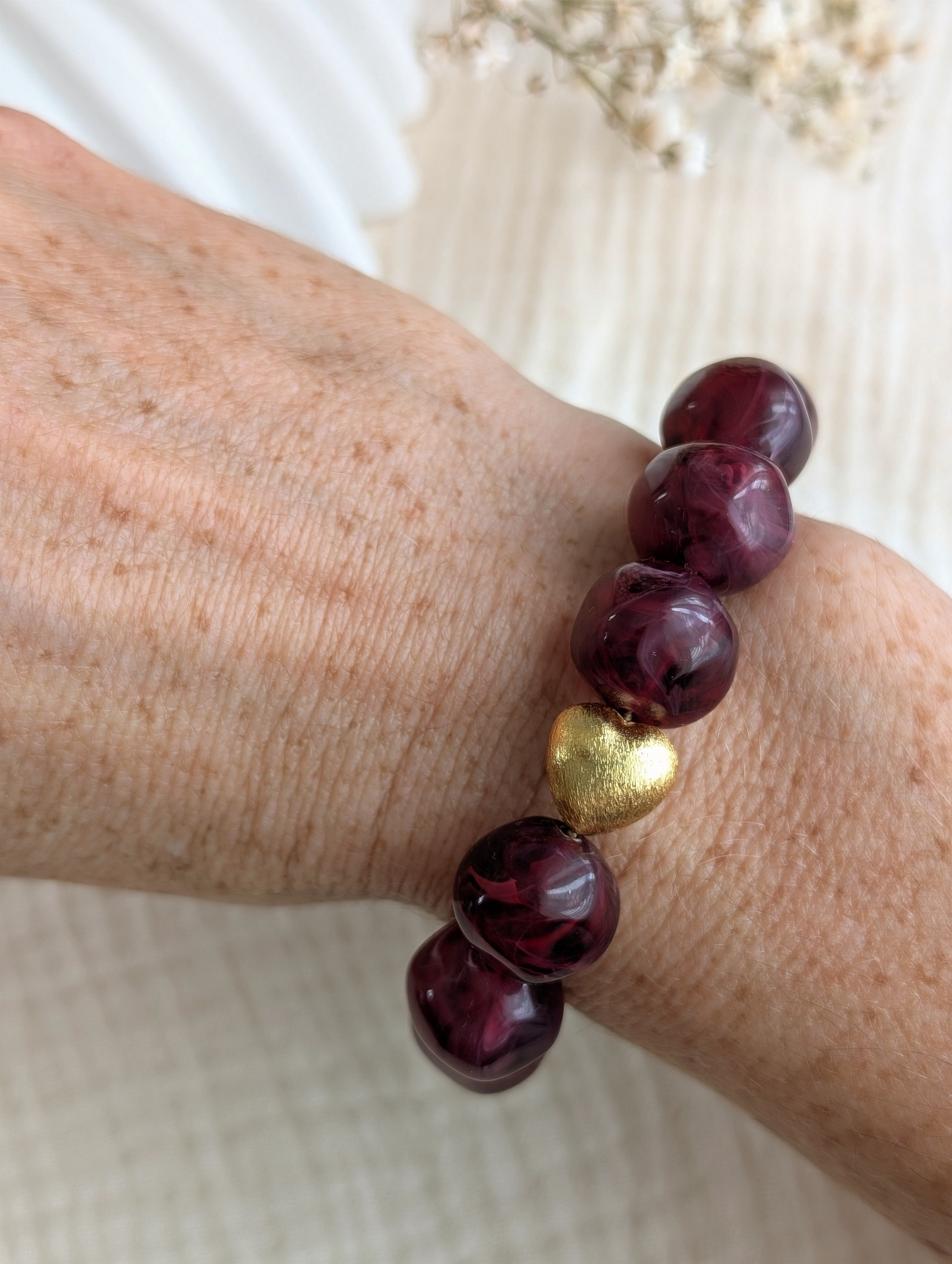 Bracelet Perles résine Adèle couleur grenat marbré et perle coeur doré brossé plaqué or porté sur poignet. Création fait main La Tête dans les Nétoiles