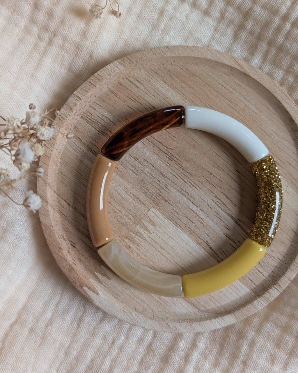 Bracelet jonc perle tube résine couleurs jaune ambre et blanc avec perle pailletée dorée sur plateau bois. Création la Tête dans les Nétoiles