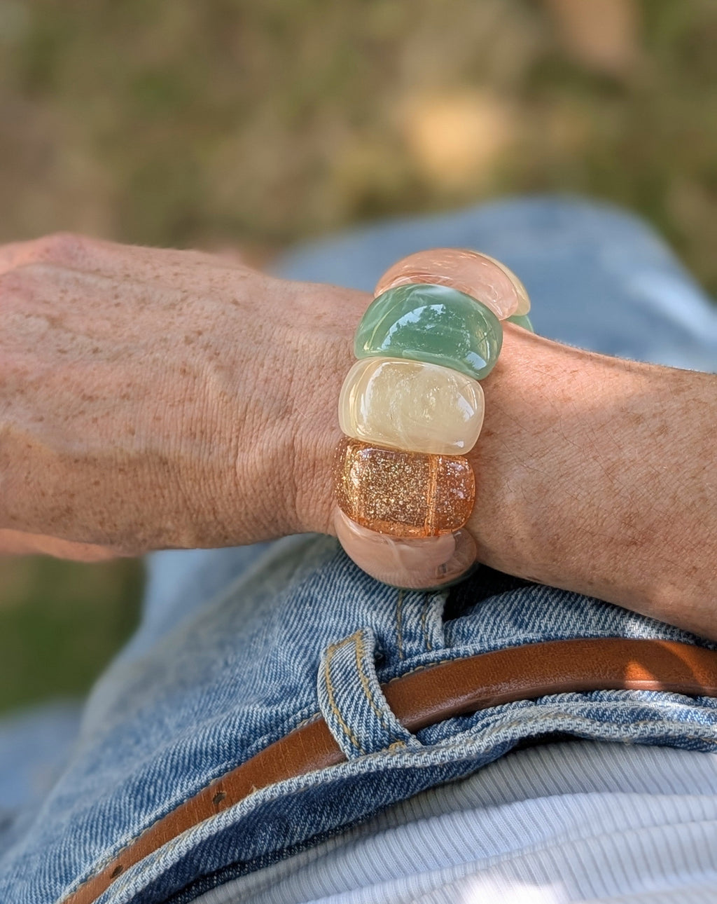 Bracelet manchette Ysée Rose vert écru champagne doré paillettes. Porté par une femme avec un short en jean. Créations artisanales La Tête dans les Nétoiles.