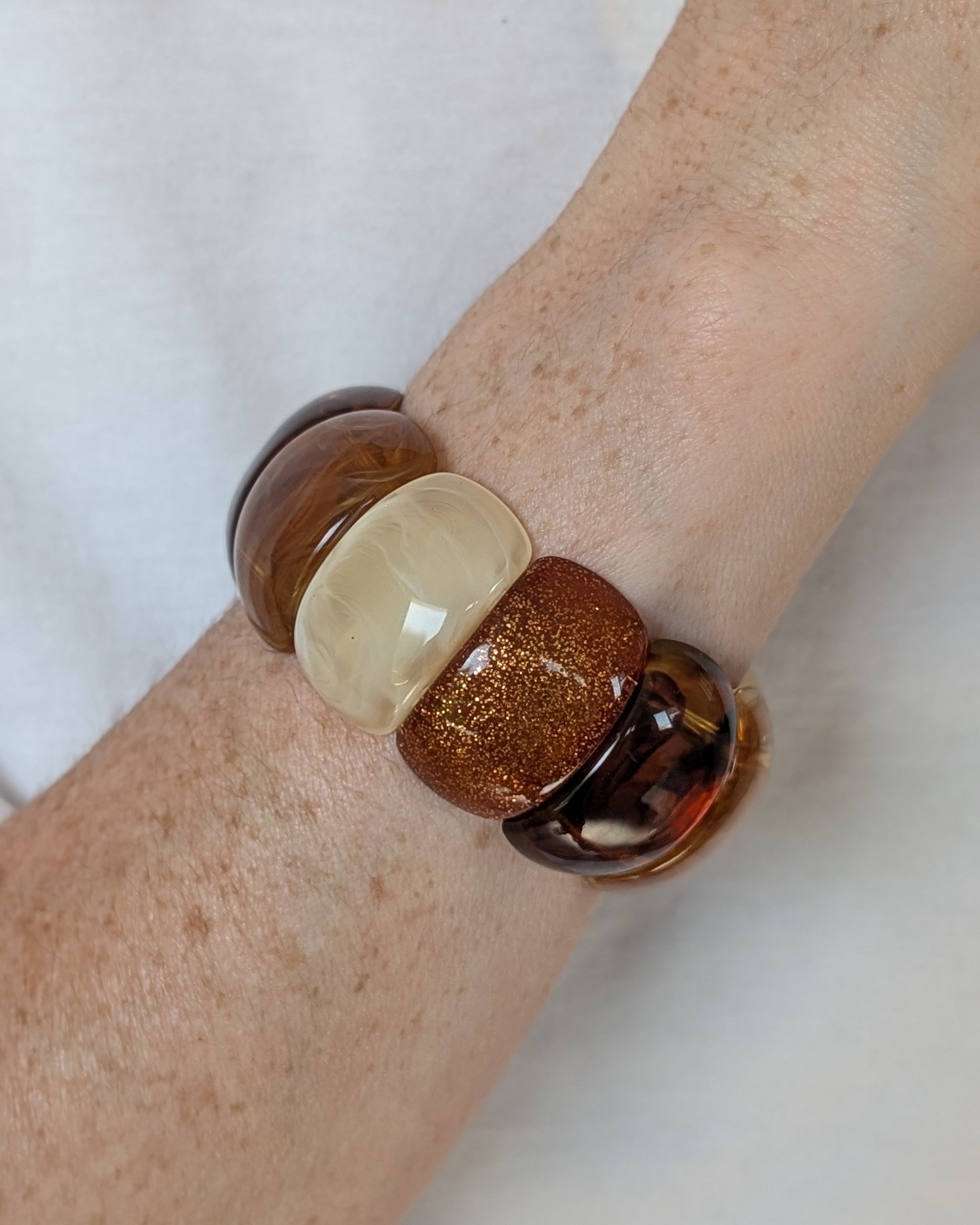 Bracelet manchette élastique Ysée miel caramel écru et glitter cuivré créations artisanales La Tête dans les Nétoiles. Porté au poignet d'une femme avec un tee shirt blanc 