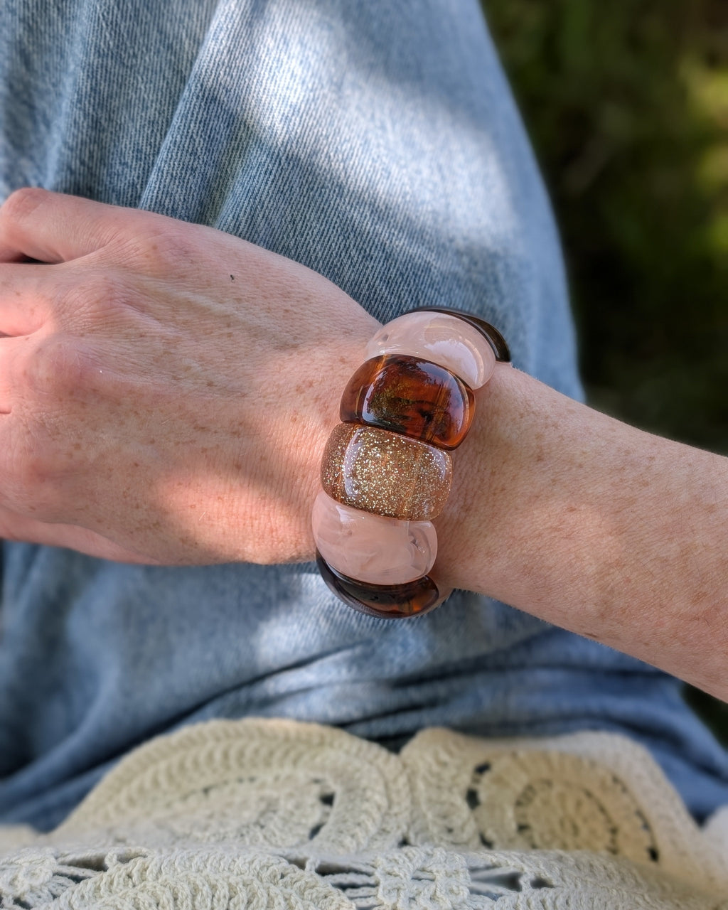 Bracelet manchette élastique Ysée Rose des sables caramel et glitter champagne. Porté par une femme à son poignet avec un jean et un haut brodé.Créations bijoux artisanaux La Tête dans les Nétoiles. Bijoux en résine 