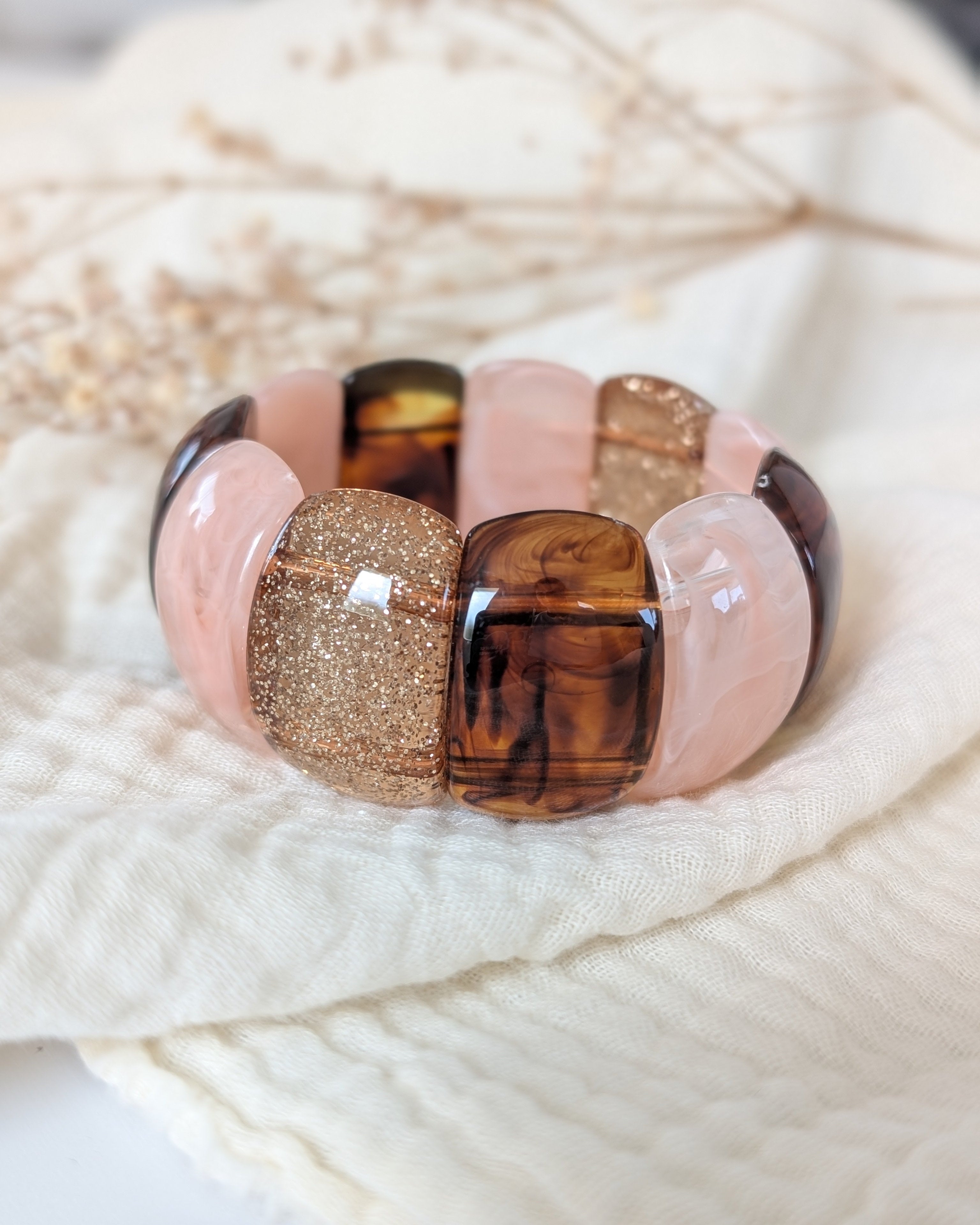 Bracelet manchette élastique Ysée Rose des sables caramel et glitter champagne. Posée sur une gaze de coton. Créations bijoux artisanaux La Tête dans les Nétoiles. Bijoux en résine 