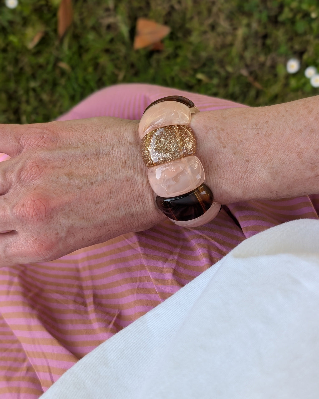 Bracelet manchette élastique Ysée Rose des sables caramel et glitter champagne. Porté par une femme avec une robe à rayures rose et ocre. Créations bijoux artisanaux La Tête dans les Nétoiles. Bijoux en résine 
