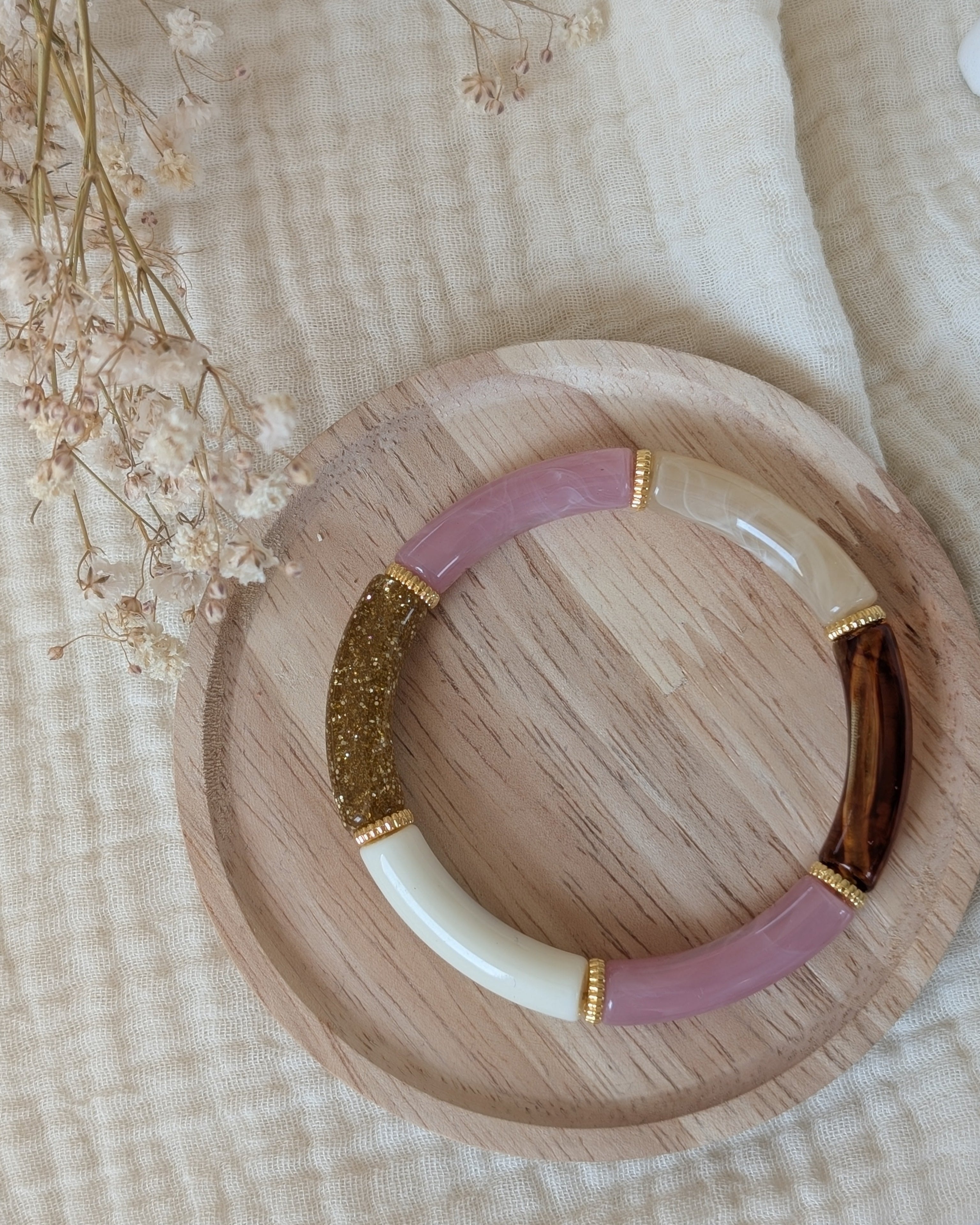 Bracelet perle tube Lison en rose doux marbré et intercalaire perle doré. Posé sur un plateau en bois. Création La Tête dans les Nétoiles