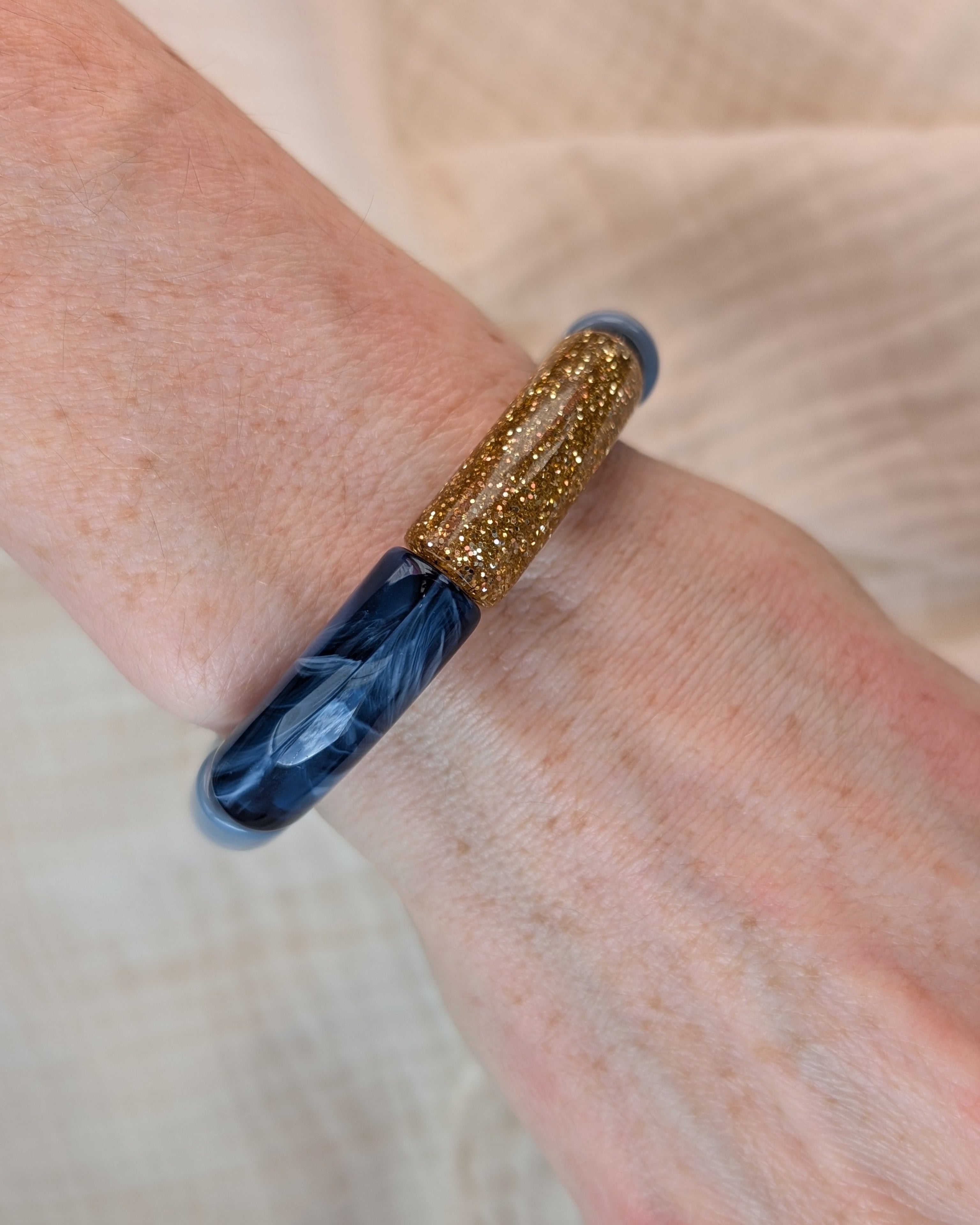 Bracelet perle tube MONA en bleu et glitter doré. Porté sur poignet de femme. Création La Tête dans les Nétoiles
