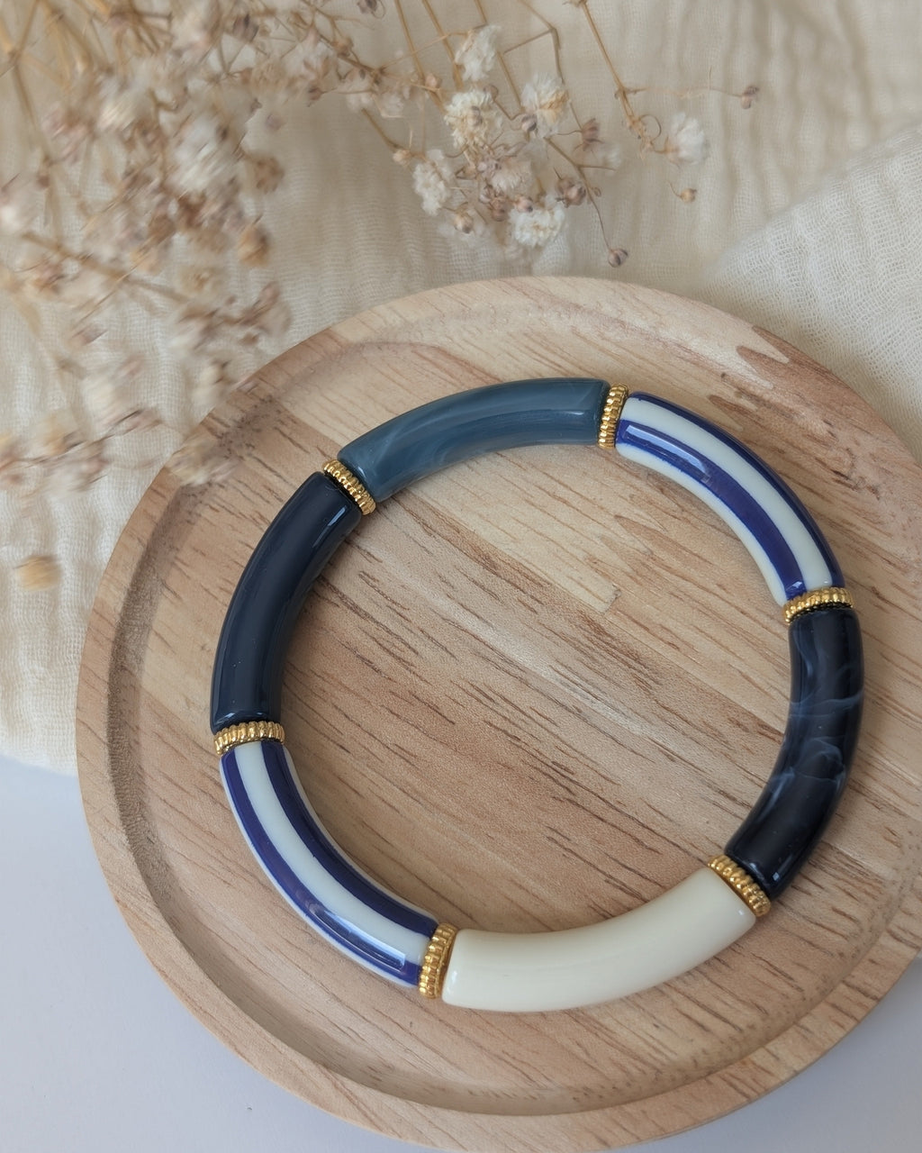Bracelet perles tube Lison rayures bleues et écru posé sur plateau en bois. Création artisanale La Tête dans les Nétoiles 