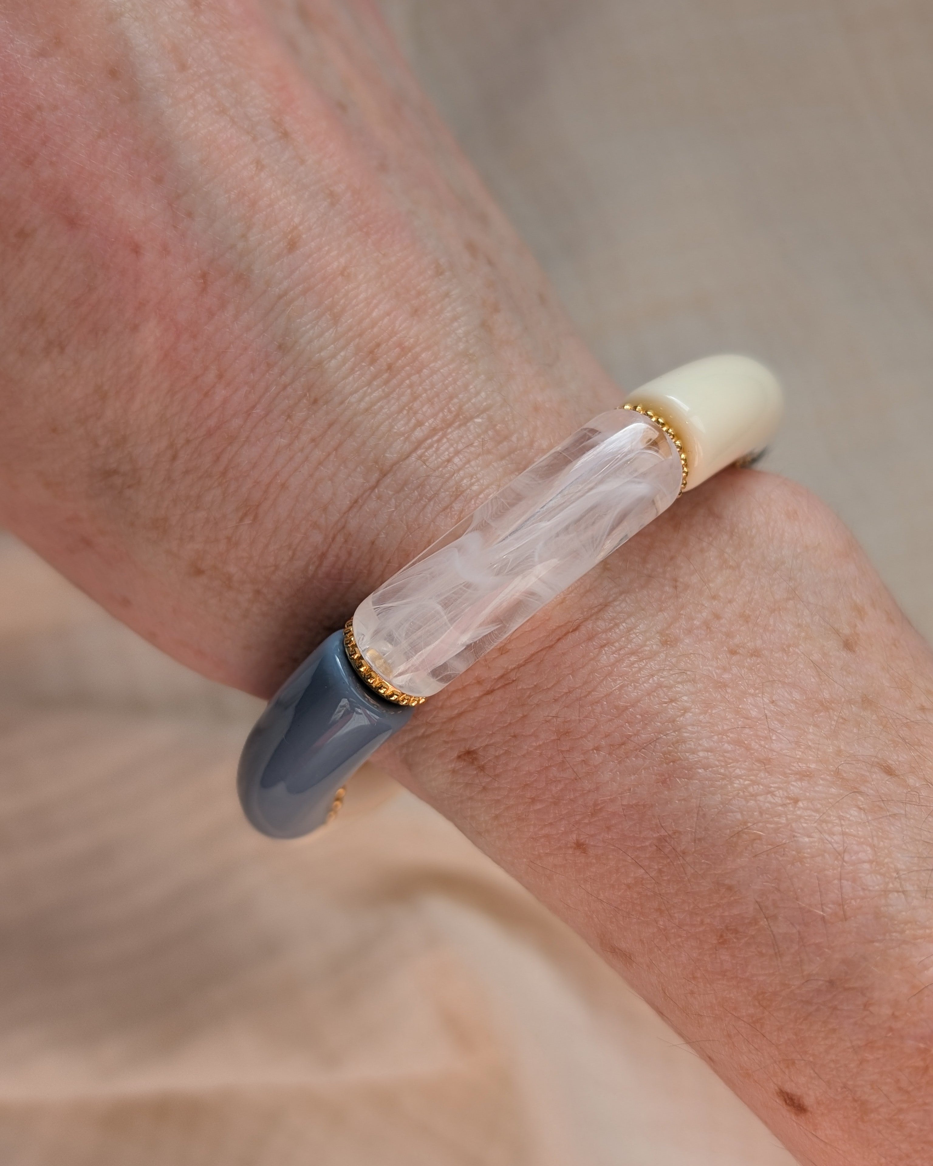Bracelet perles tube Marie bleu, écru, blanc transparent et glitter doréavec perles intercalaires dorées haute qualité. Porté au poignet d'une femme. Création La Tête dans les nétoiles