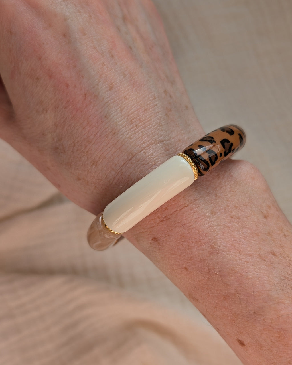 Bracelet perles tube Marie coloris léopard et tons naturels avec perles intercalaires dorées hautes qualité. Porté au poignet d'une femme. Création La Tête dans les Nétoiles