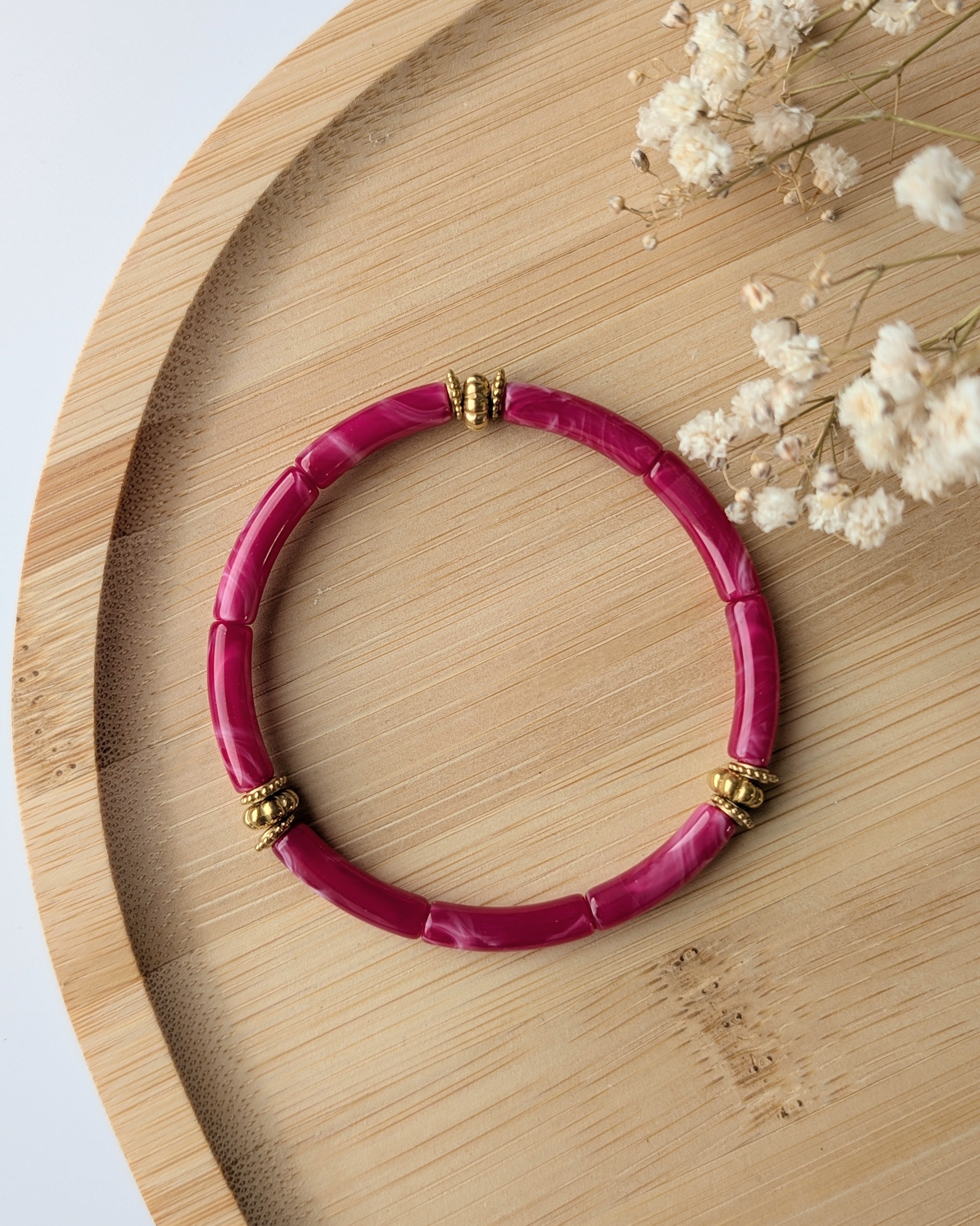 Bracelet perles tube rose fuchia marbré diamètre 5 mm sur support en bois. Détails perles dorées en acier inoxydable doré. Création la Tête dans les Nétoiles