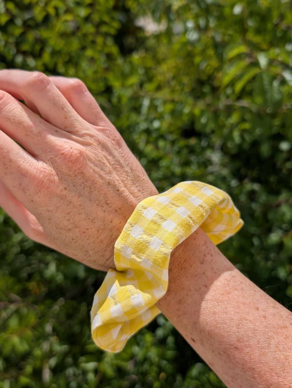 Chouchou motif vichy jaune et blanc porté au poignet d'une femme. Créations artisanales La Tête dans les Nétoiles