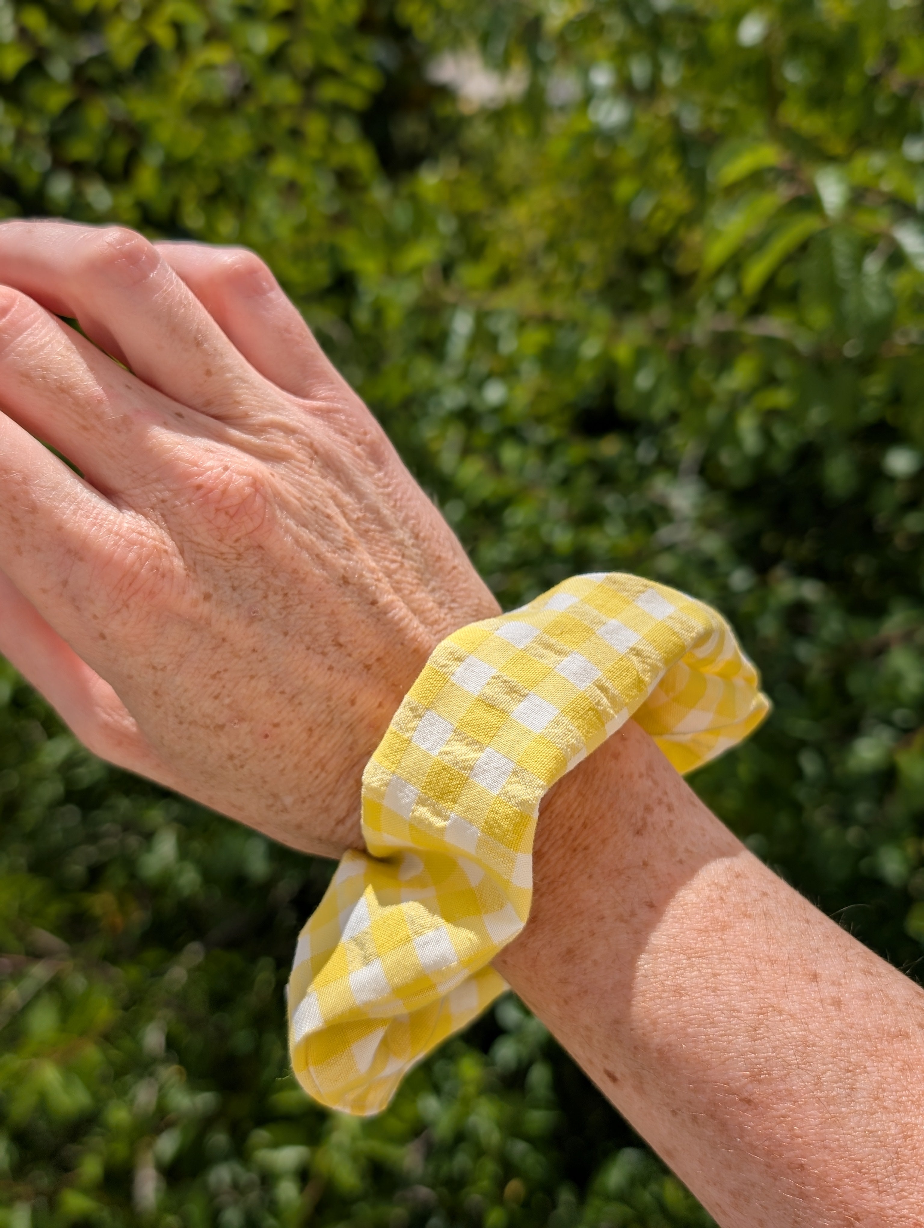 Chouchou motif vichy jaune et blanc porté au poignet d'une femme. Créations artisanales La Tête dans les Nétoiles