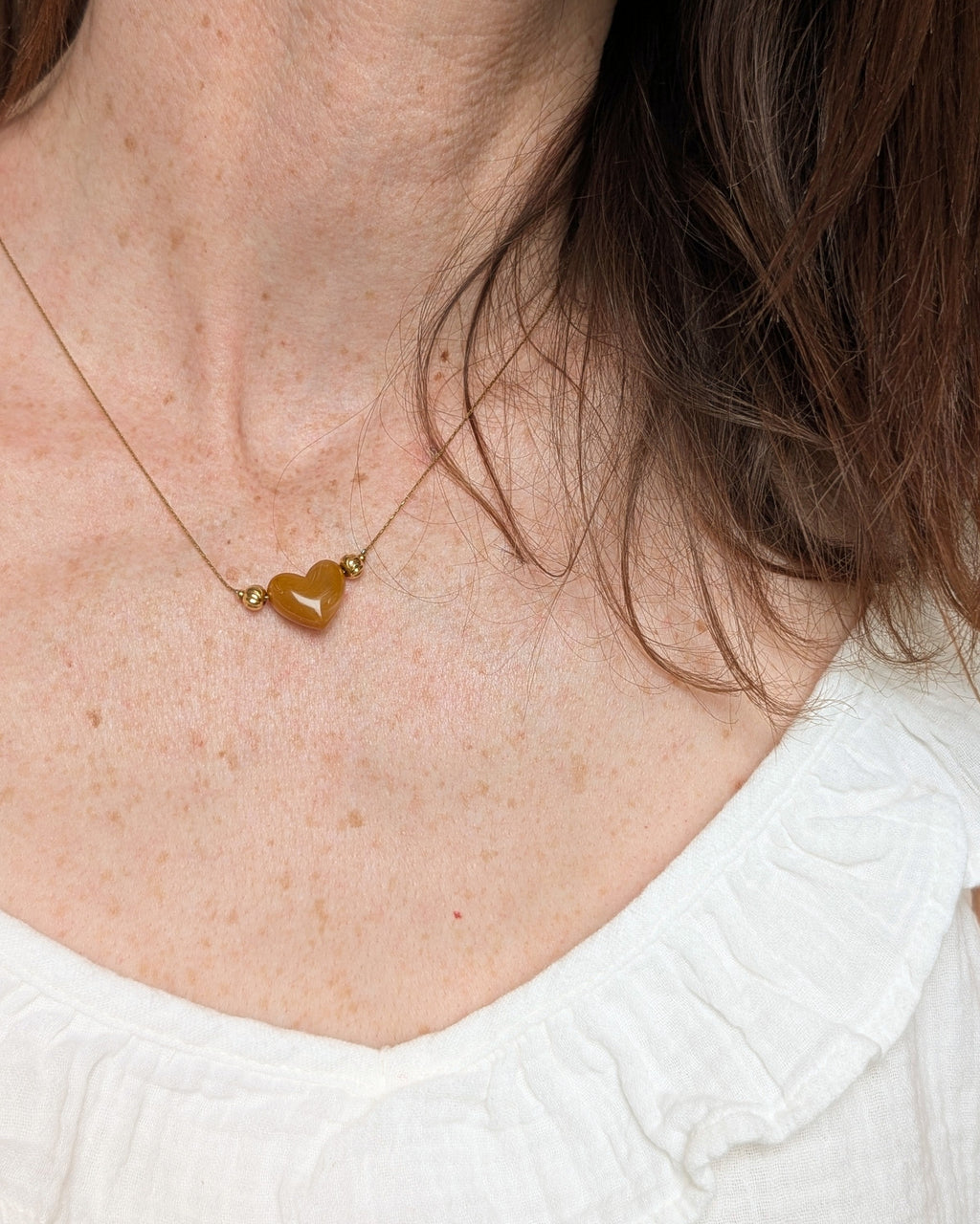 Collier Aimée perle coeur en résine abricot marbré et acier inoxydable doré. Porté par une femme. Créations faits main La Tête dans les Nétoiles