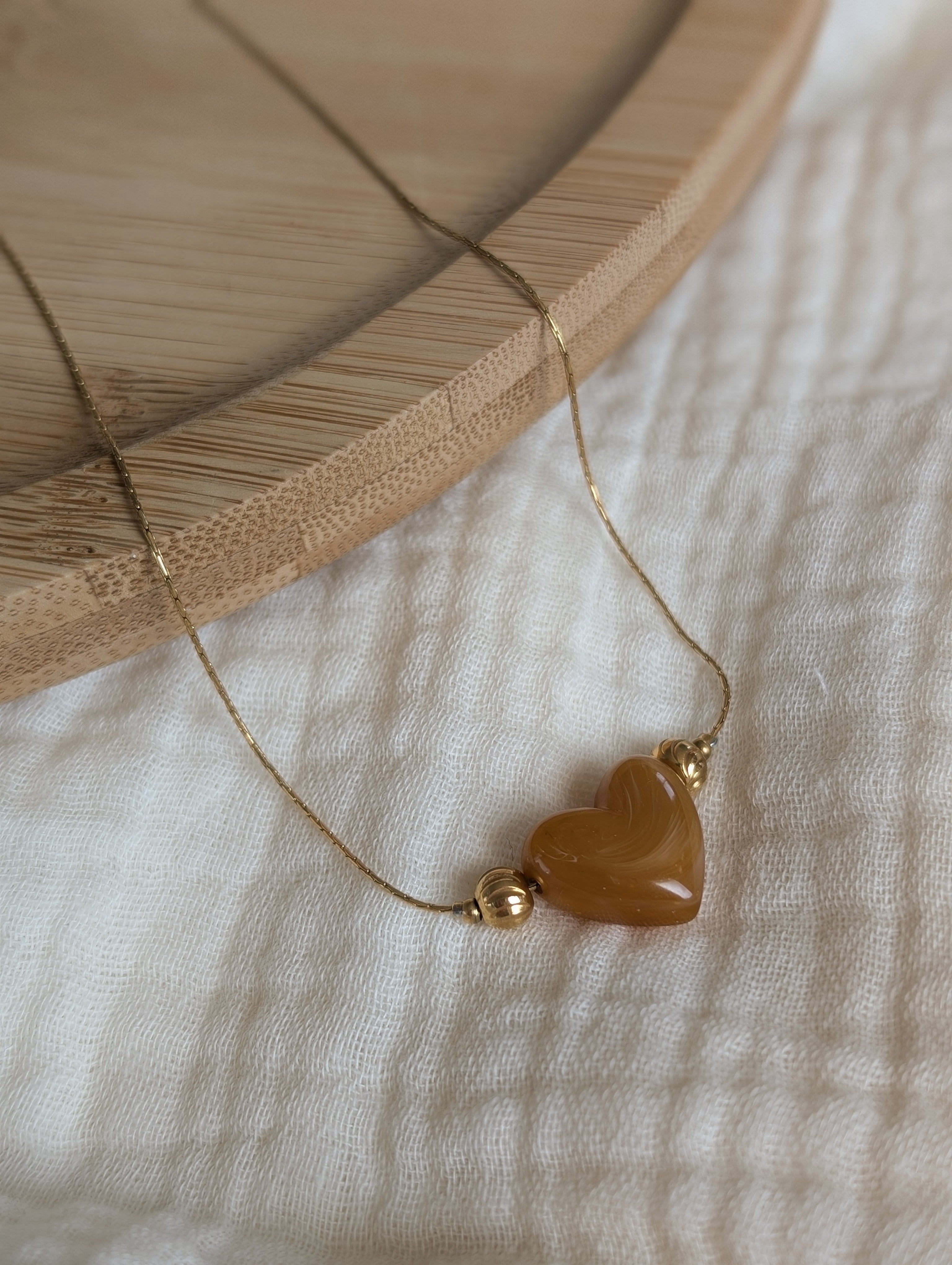 Collier Aimée perle coeur en résine abricot marbré et acier inoxydable doré. Posé sur plateau en bois et gaze de coton écru. Créations faits main La Tête dans les Nétoiles