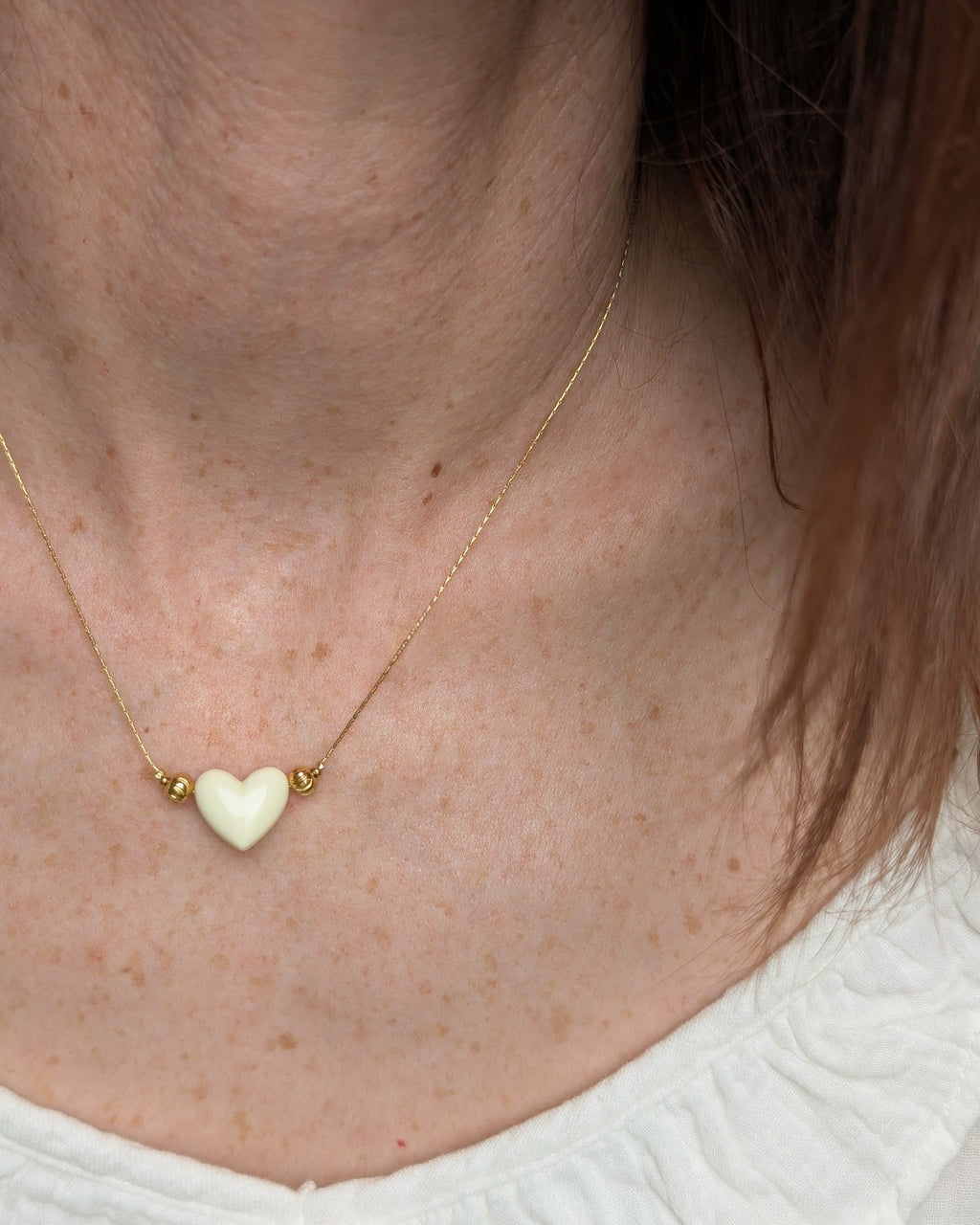 Collier Aimée perle coeur en résine écru et acier inoxydable doré. Porté par une femme. Créations faits main La Tête dans les Nétoiles