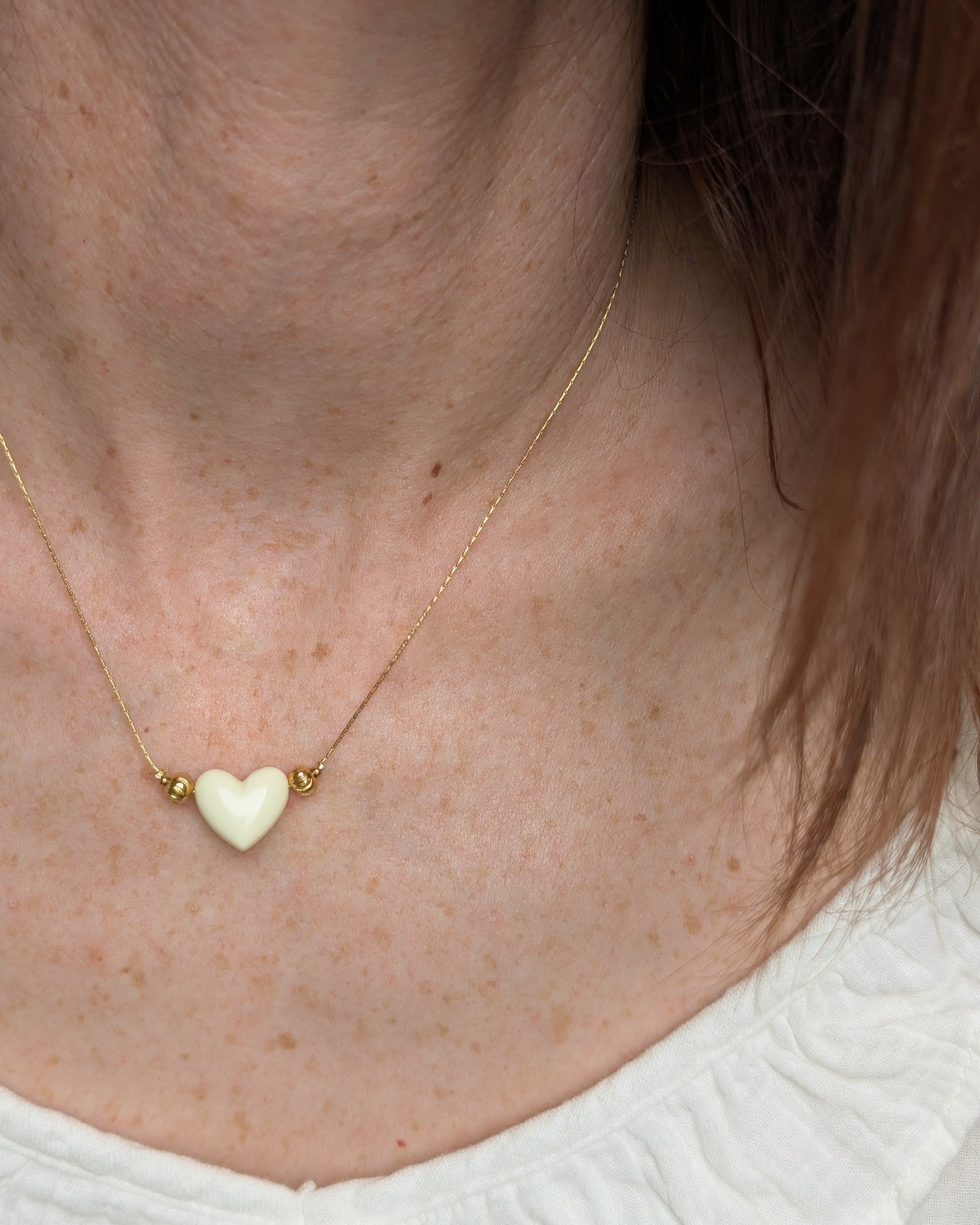 Collier Aimée perle coeur en résine écru et acier inoxydable doré. Porté par une femme. Créations faits main La Tête dans les Nétoiles