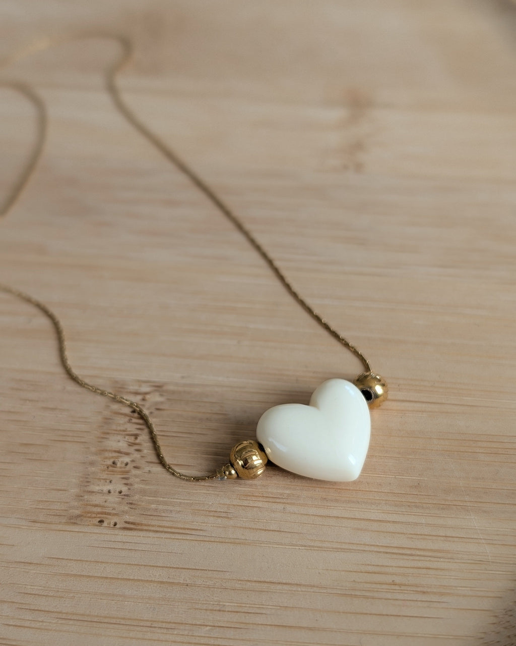 Collier Aimée perle coeur en résine écru et acier inoxydable doré. Posé sur plateau en bois. Créations faits main La Tête dans les Nétoiles