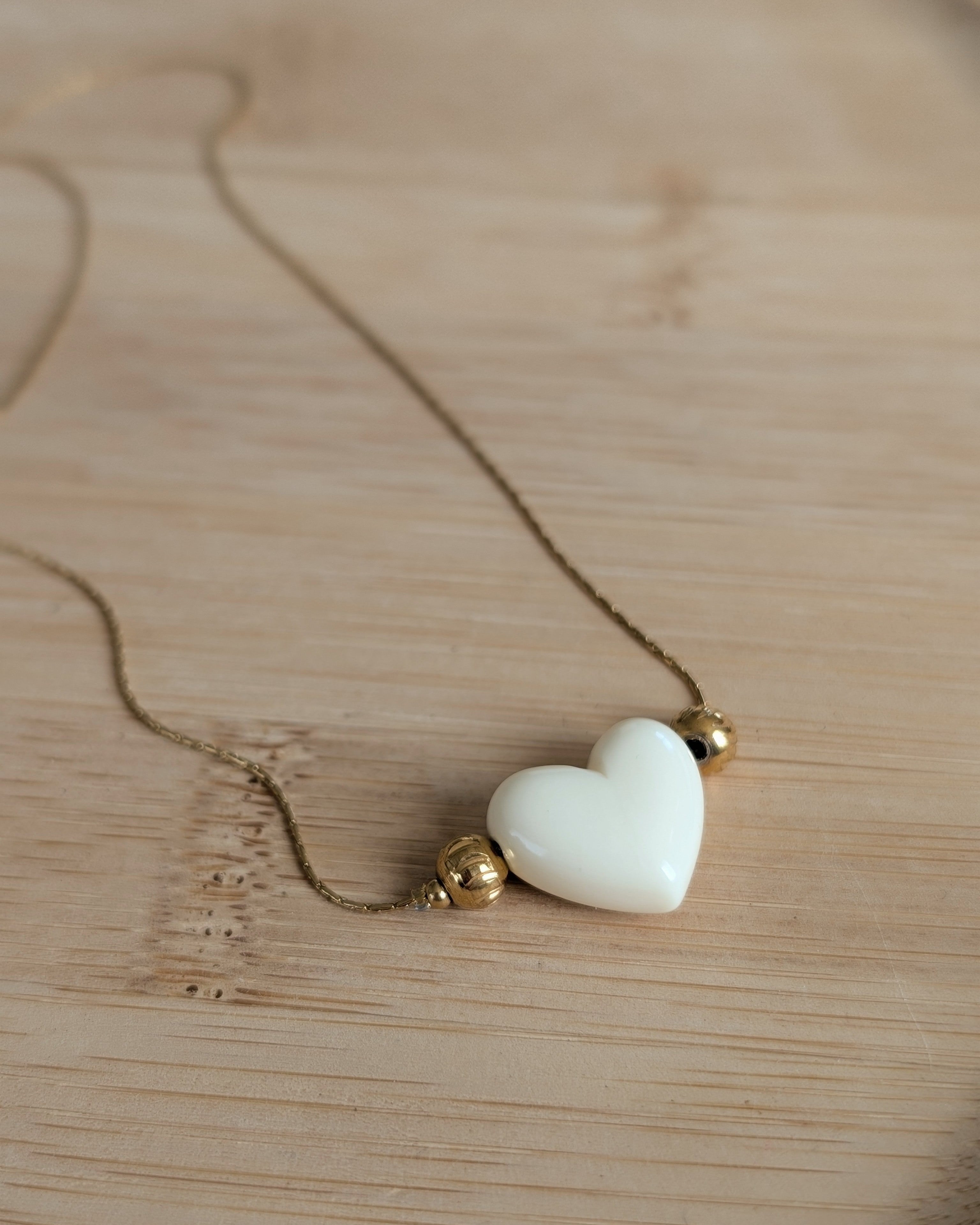 Collier Aimée perle coeur en résine écru et acier inoxydable doré. Posé sur plateau en bois. Créations faits main La Tête dans les Nétoiles