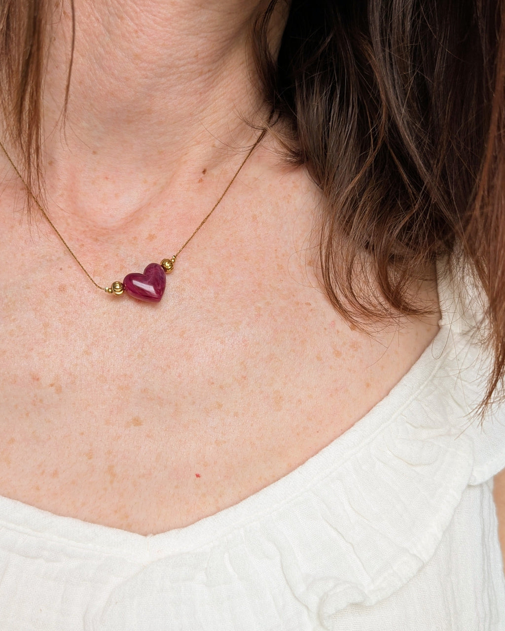 Collier Aimée perle coeur en résine grenat marbré et acier inoxydable doré. Porté par une femme. Créations faits main La Tête dans les Nétoiles