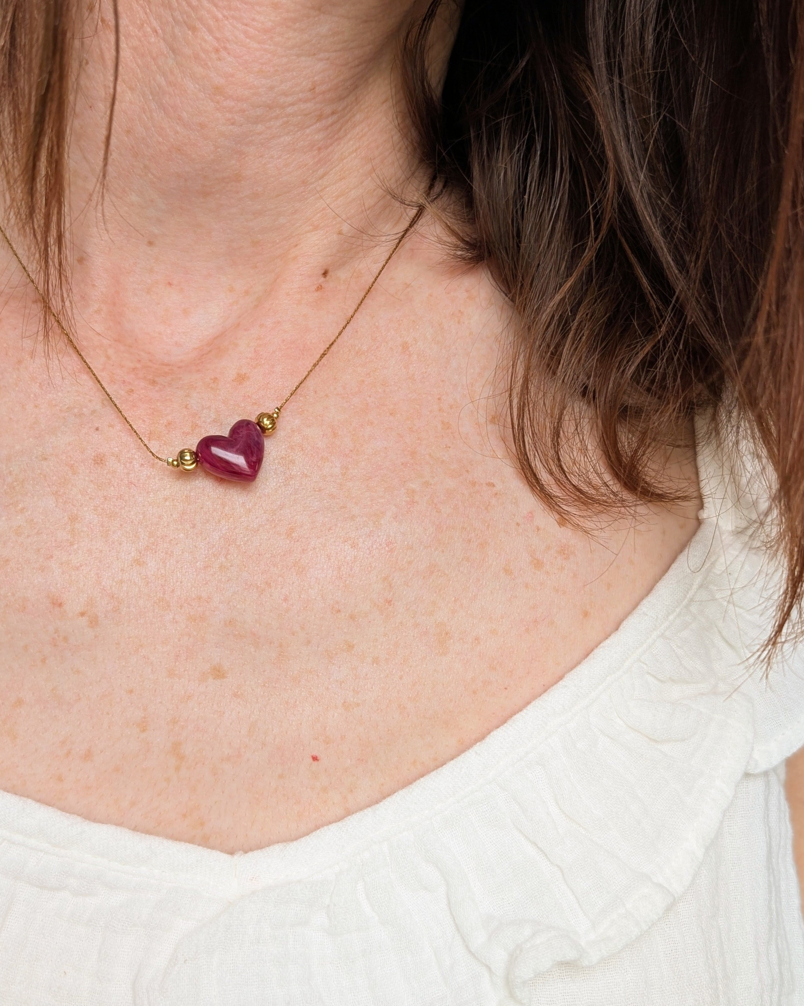 Collier Aimée perle coeur en résine grenat marbré et acier inoxydable doré. Porté par une femme. Créations faits main La Tête dans les Nétoiles