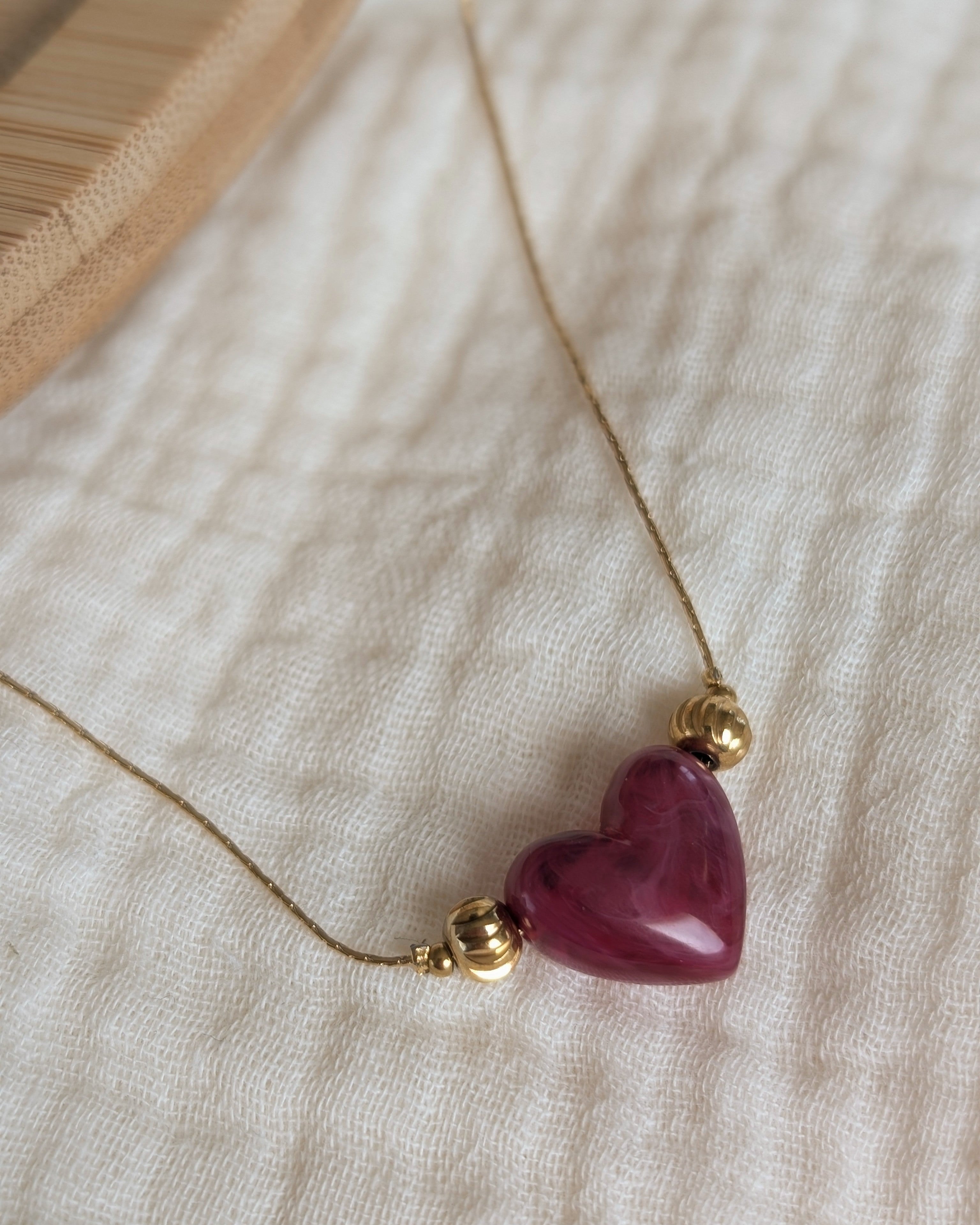Collier Aimée perle coeur en résine grenat marbré et acier inoxydable doré. Posé sur gaze de coton écru. Créations faits main La Tête dans les Nétoiles