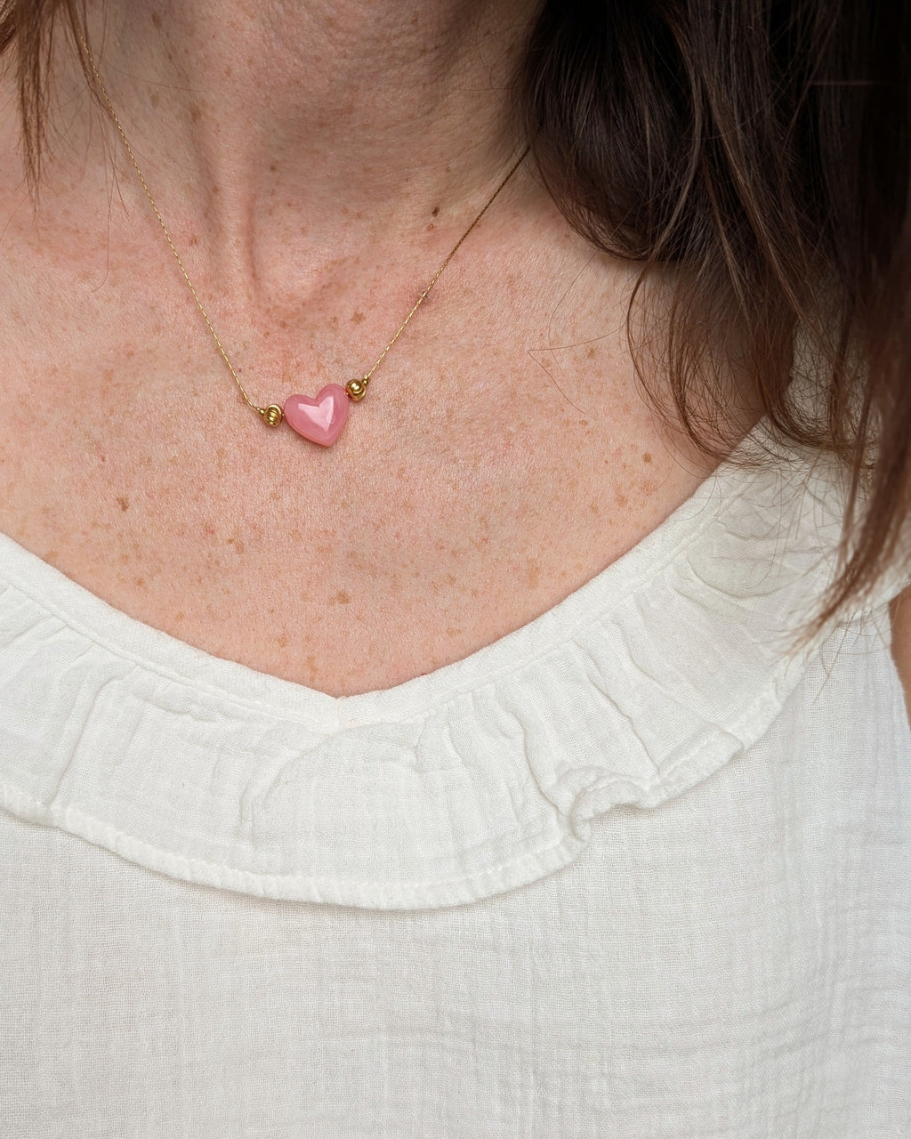 Collier Aimée perle coeur en résine rose tendre et acier inoxydable doré porté par une femme. Création fait main La Tête dans les Nétoiles